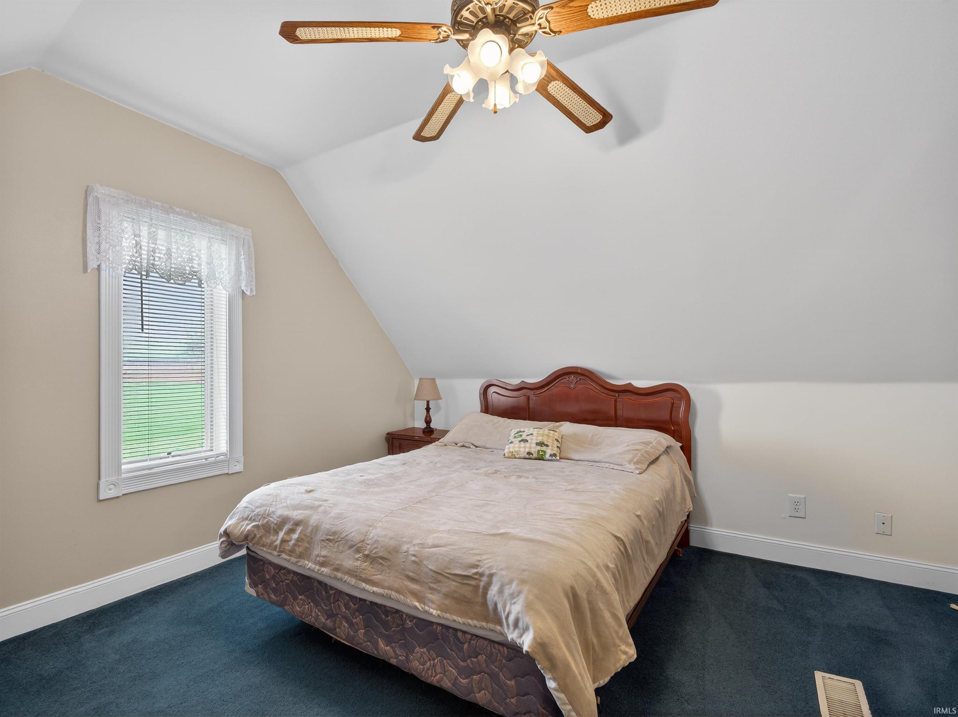 Bedroom featuring vaulted ceiling, dark carpet, and a ceiling fan