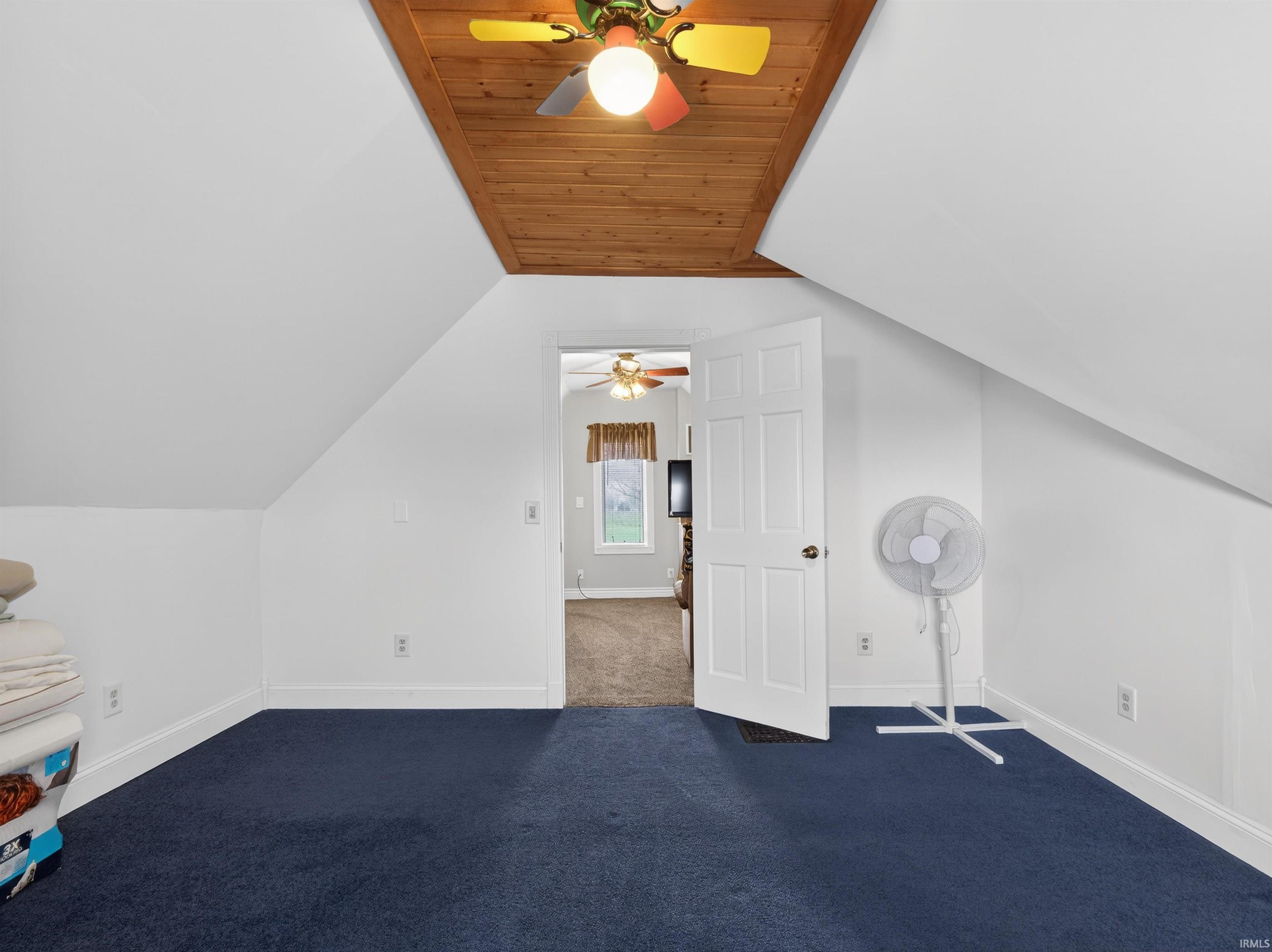 Additional living space featuring dark carpet, lofted ceiling, and ceiling fan