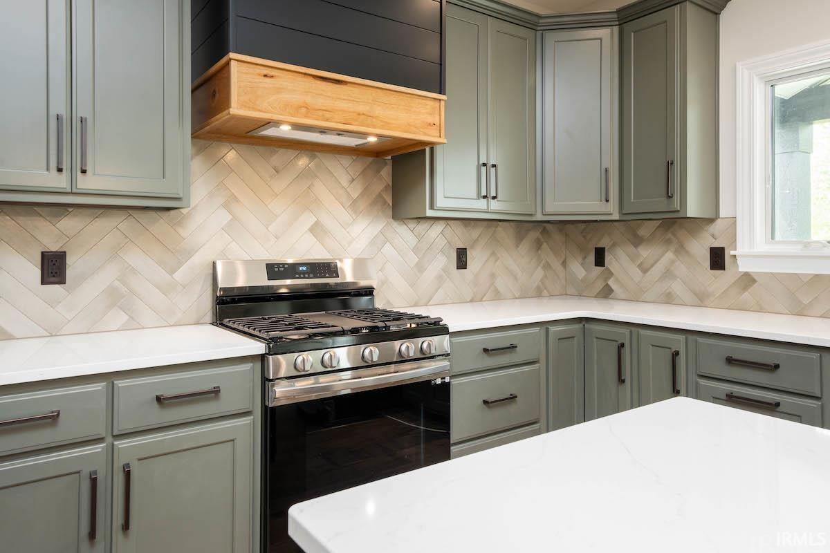 Kitchen featuring stainless steel gas stove, tasteful backsplash, and light stone countertops
