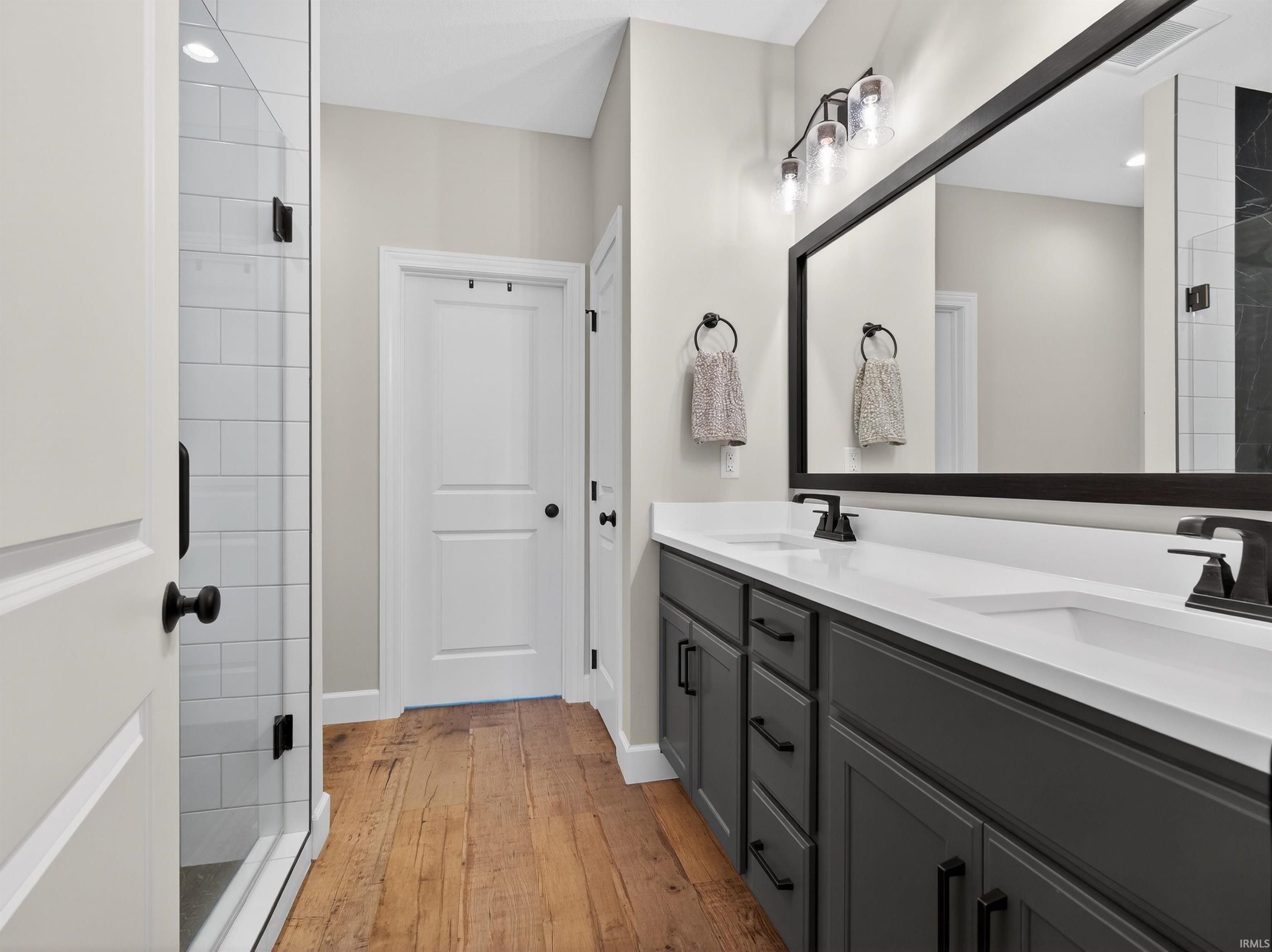 Bathroom featuring double vanity, light wood-style floors, and a tile shower
