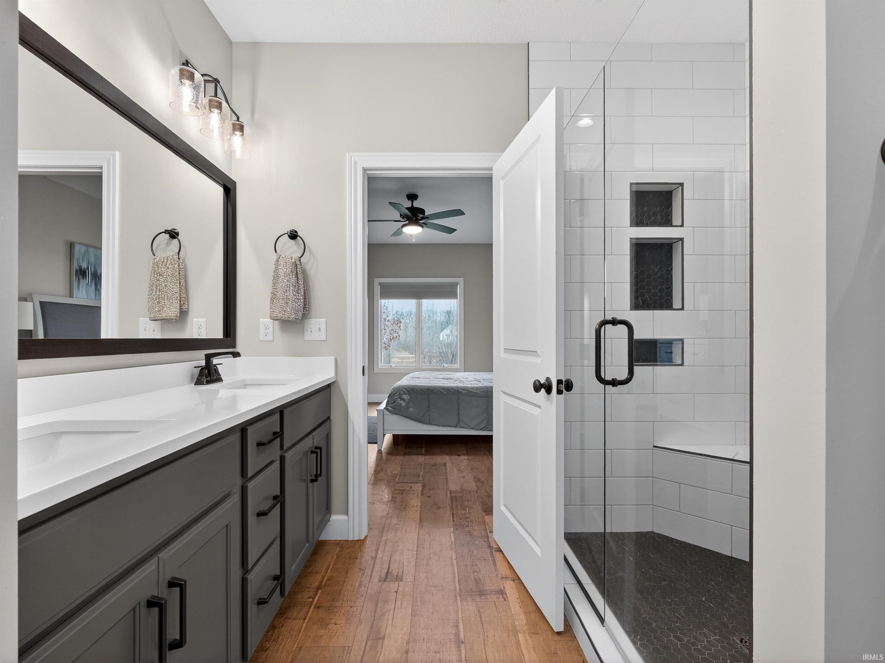 Full bath featuring double vanity, a shower stall, ensuite bath, light wood finished floors, and a ceiling fan