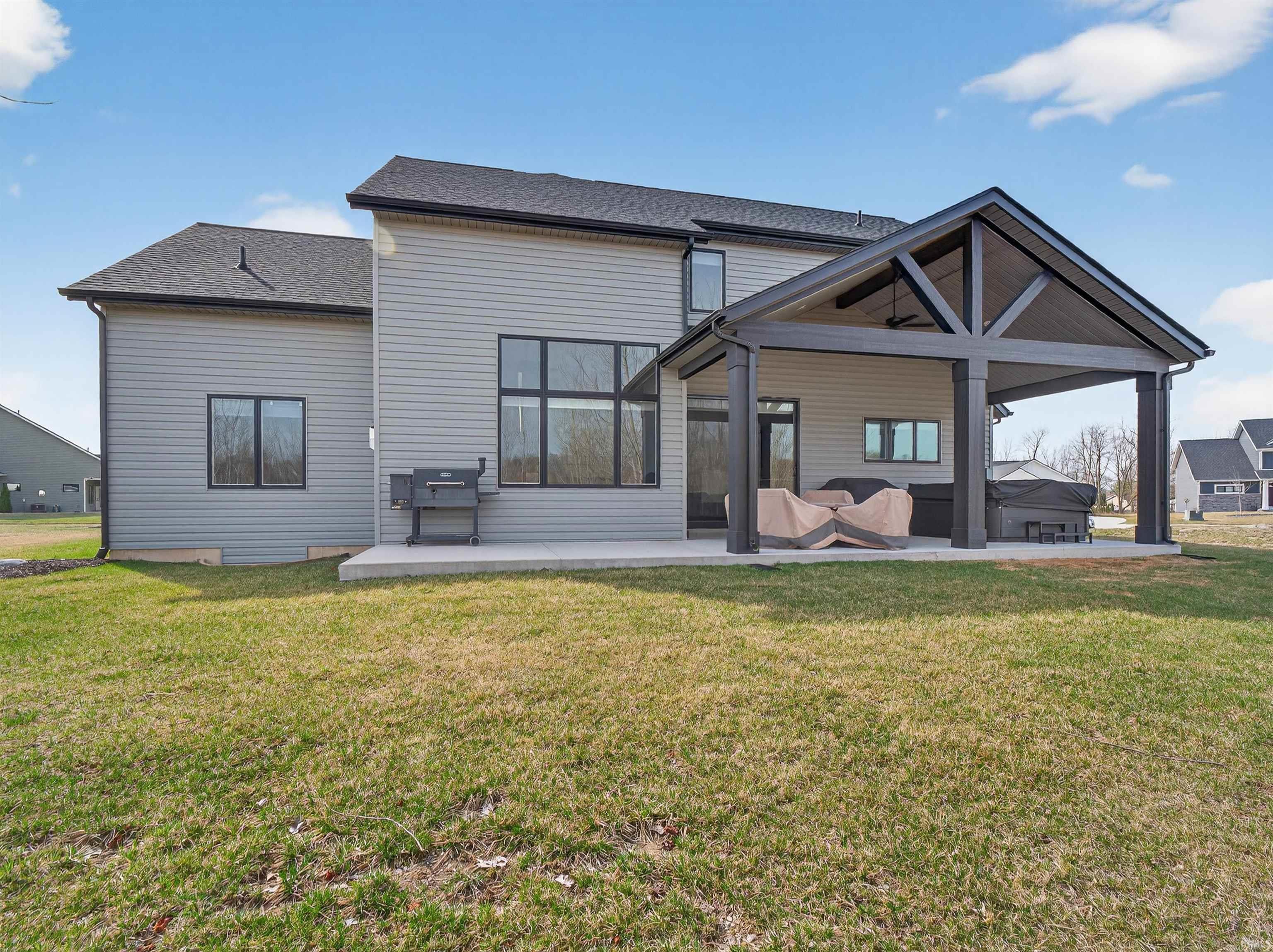 Rear view of house featuring a patio area, a lawn, and a shingled roof