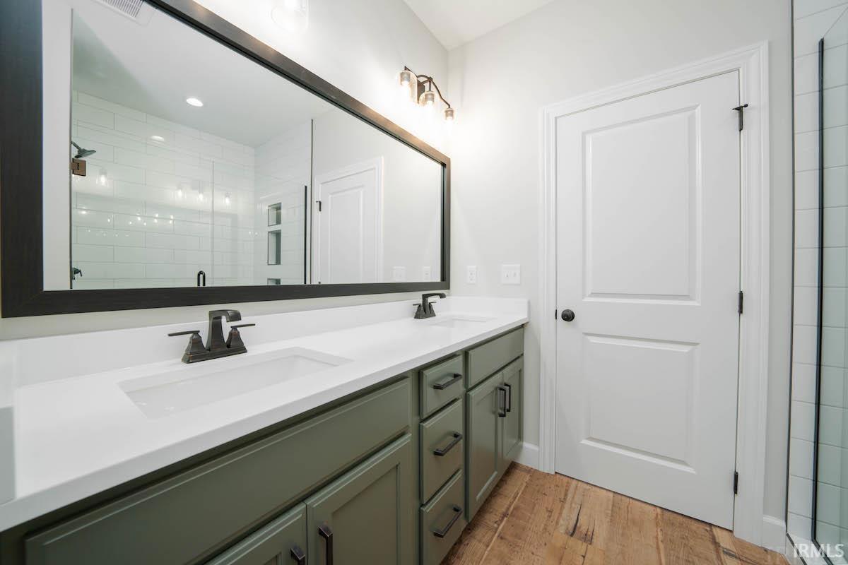 Bathroom with double vanity, light wood finished floors, and a shower stall