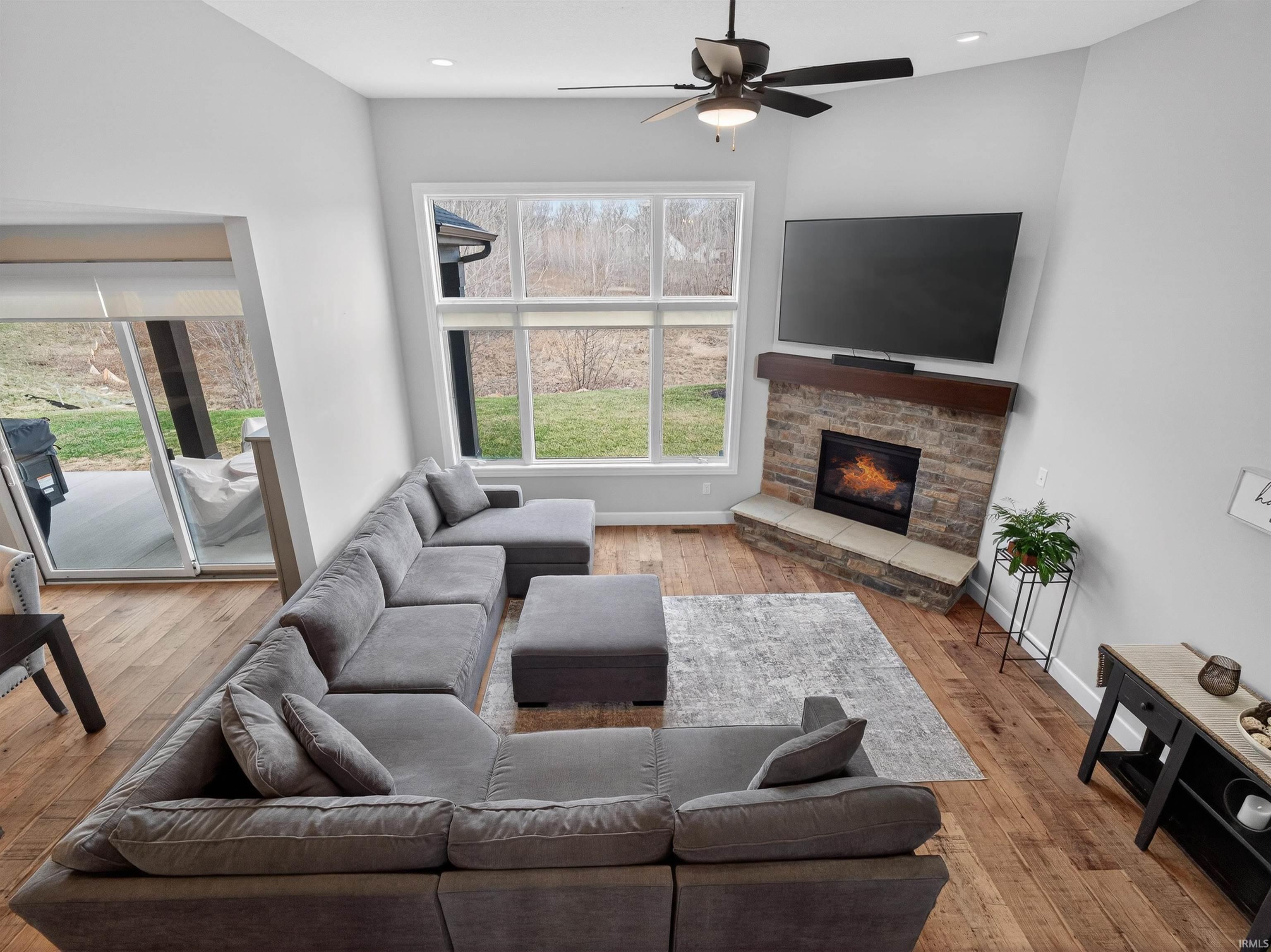 Living room with a ceiling fan, light wood finished floors, and a stone fireplace