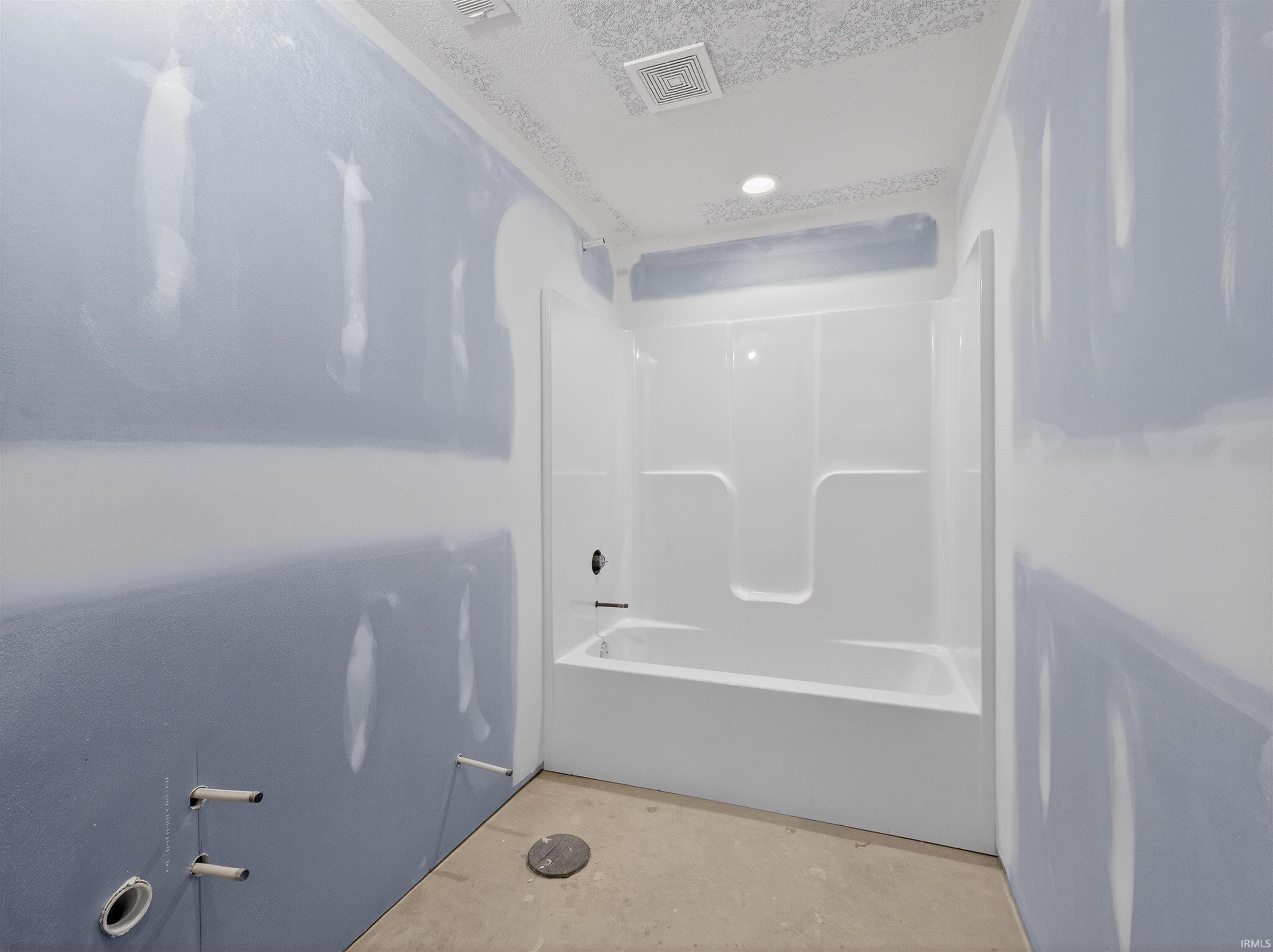 Bathroom featuring unfinished concrete flooring, bathtub / shower combination, and recessed lighting