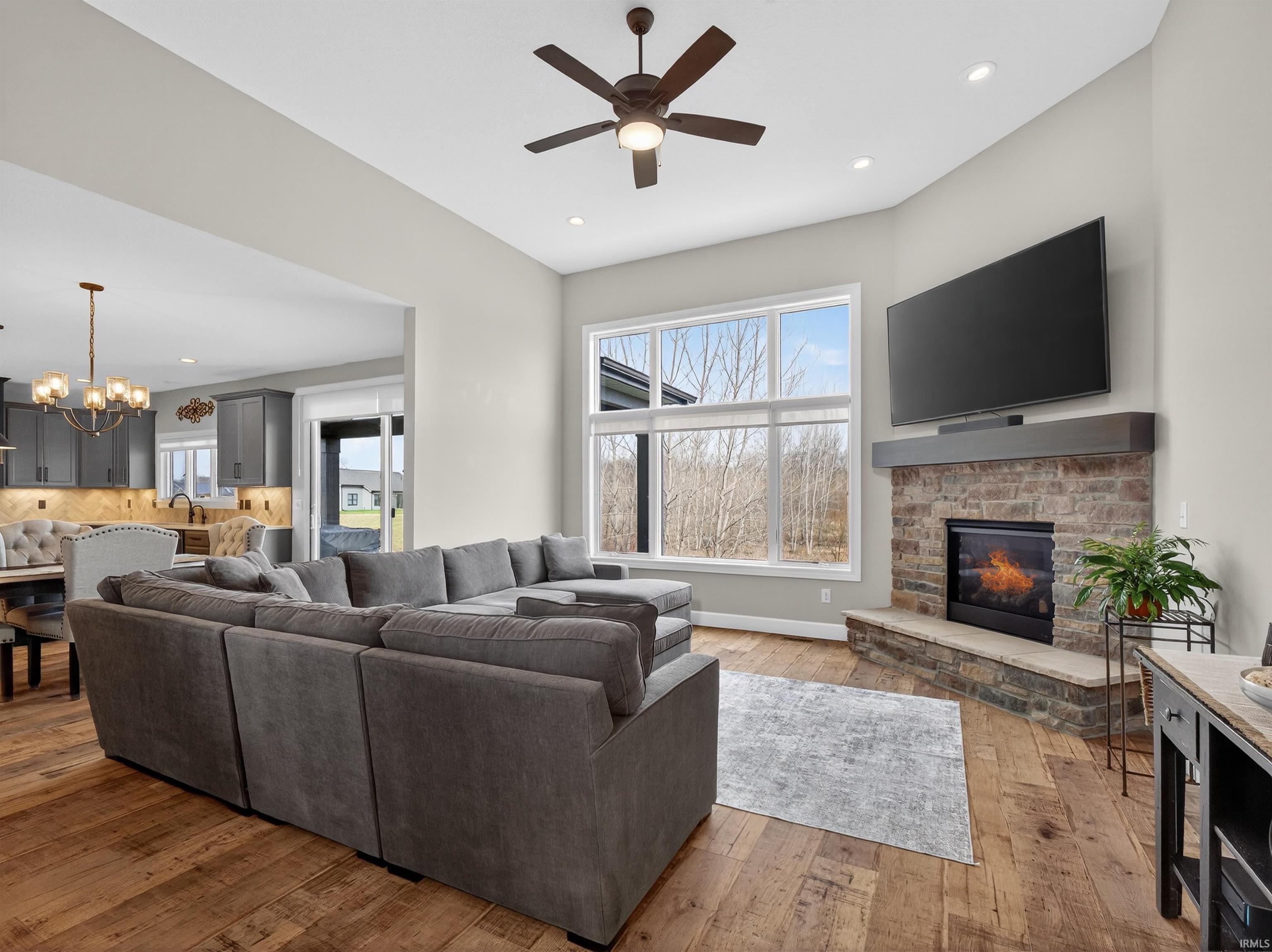 Living room featuring hanging lights, light wood-type flooring, ceiling fan, a fireplace, and healthy amount of natural light
