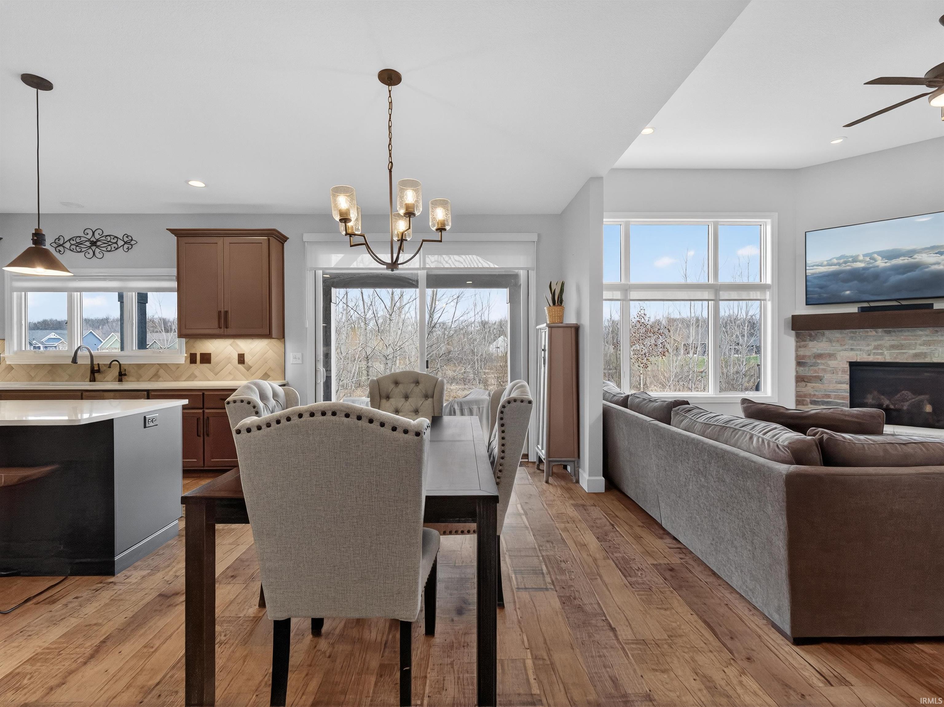 Dining area with light wood-type flooring, suspended lighting, ceiling fan, and a stone fireplace