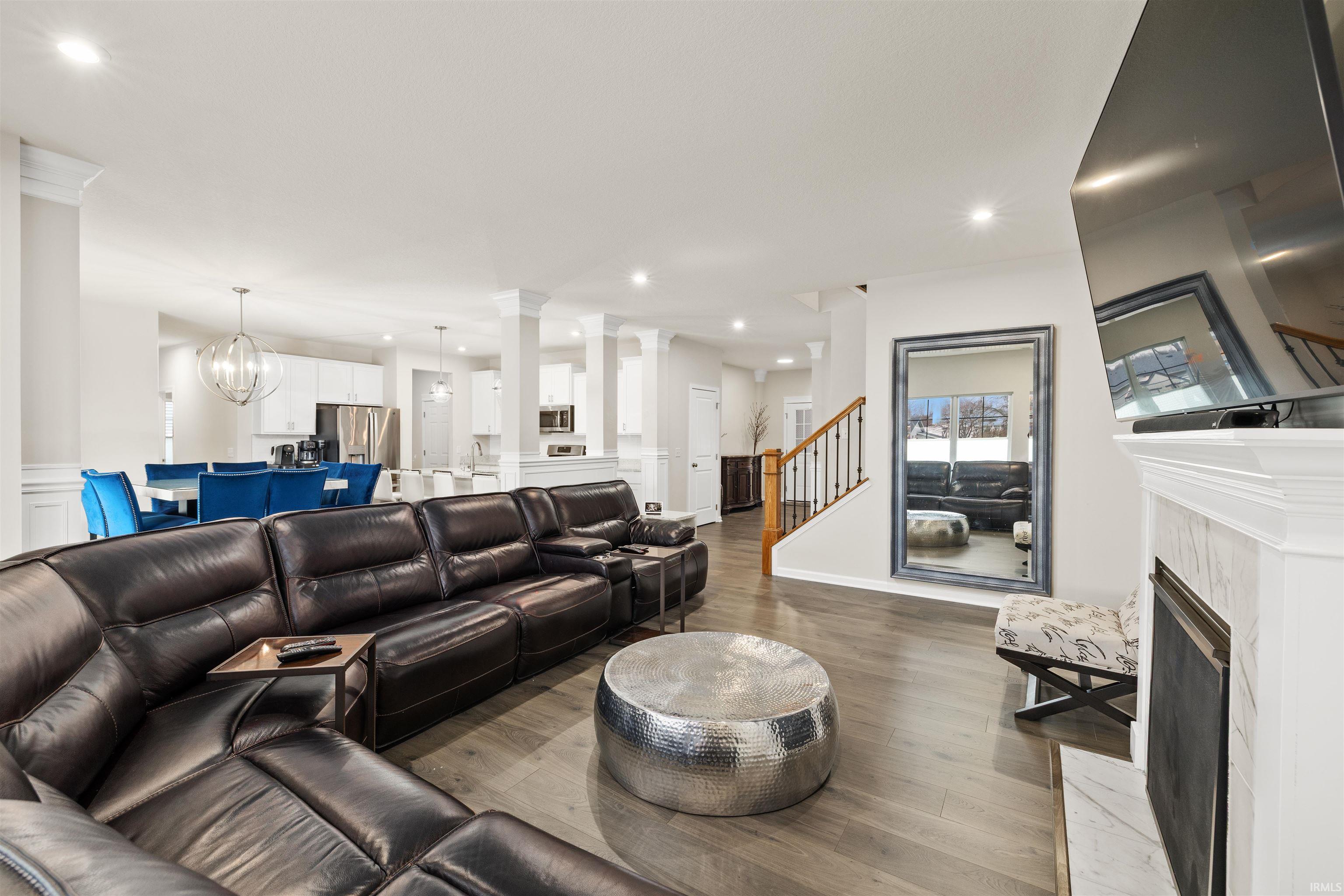 Living area featuring decorative columns, suspended lighting, dark wood finished floors, and a high end fireplace