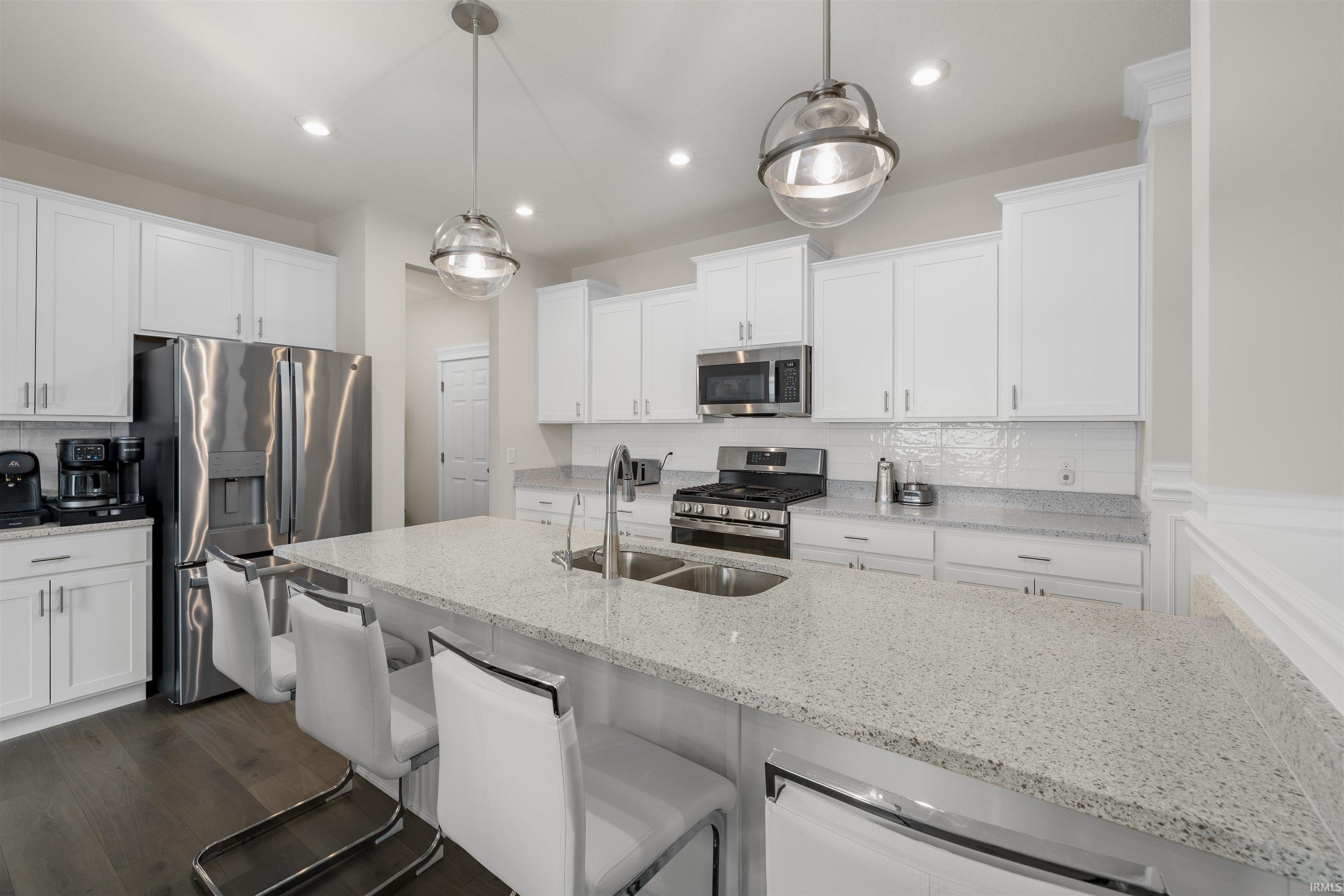 Kitchen with decorative backsplash, a kitchen bar, stainless steel appliances, light stone counters, and white cabinets