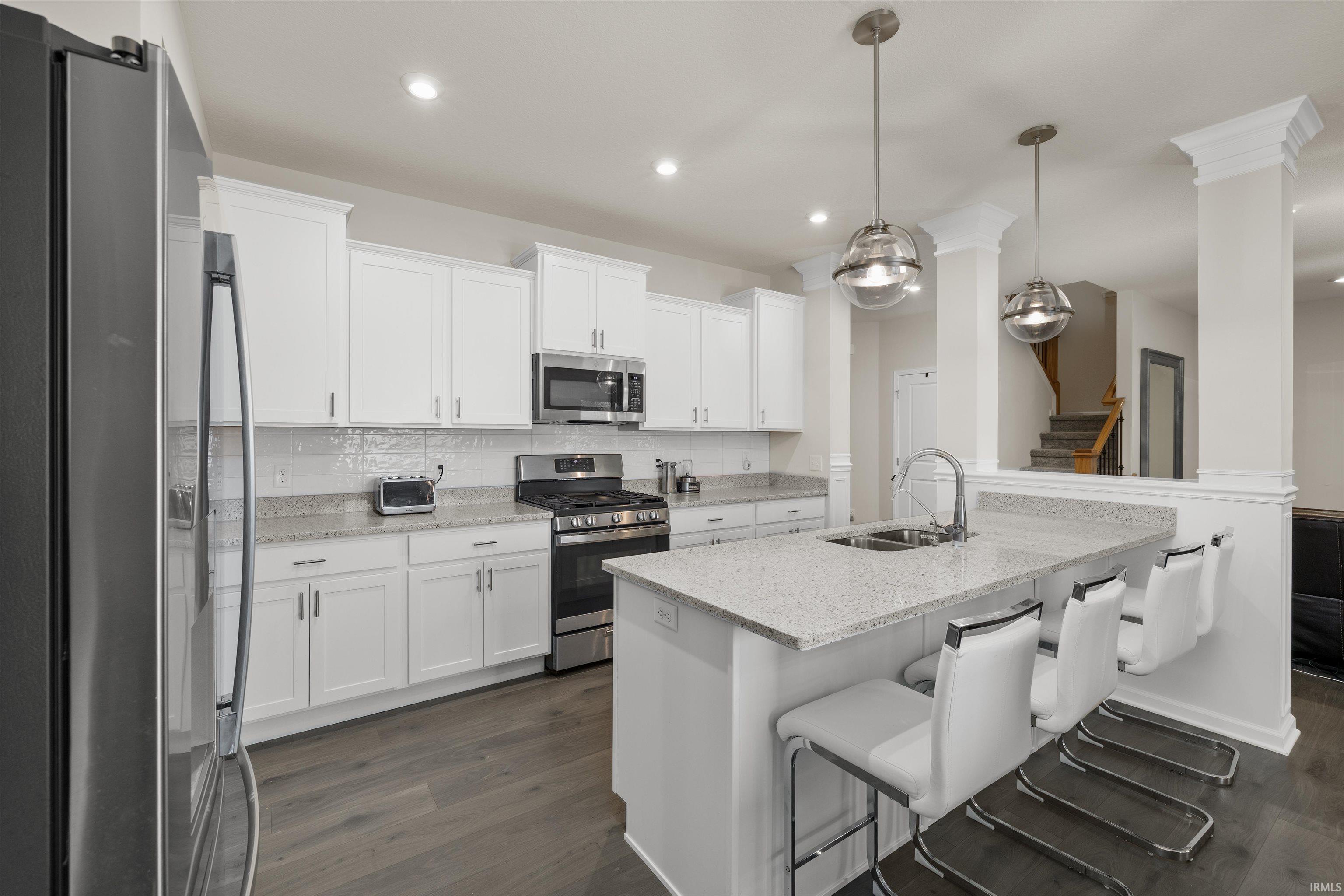 Kitchen with stainless steel appliances, white cabinets, light stone countertops, decorative backsplash, and dark wood-type flooring
