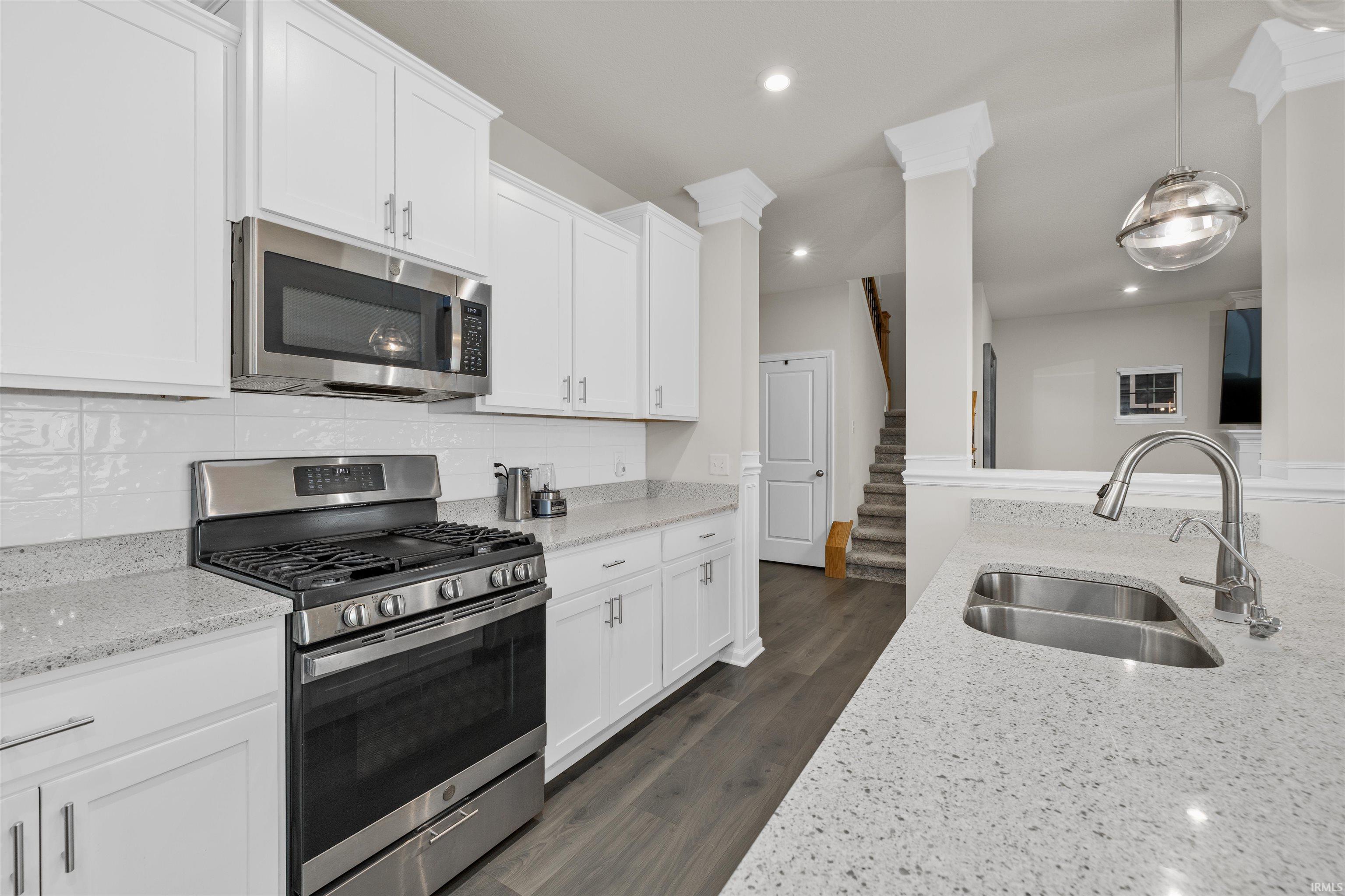 Kitchen with stainless steel appliances, white cabinetry, hanging light fixtures, light stone countertops, and dark wood-style flooring