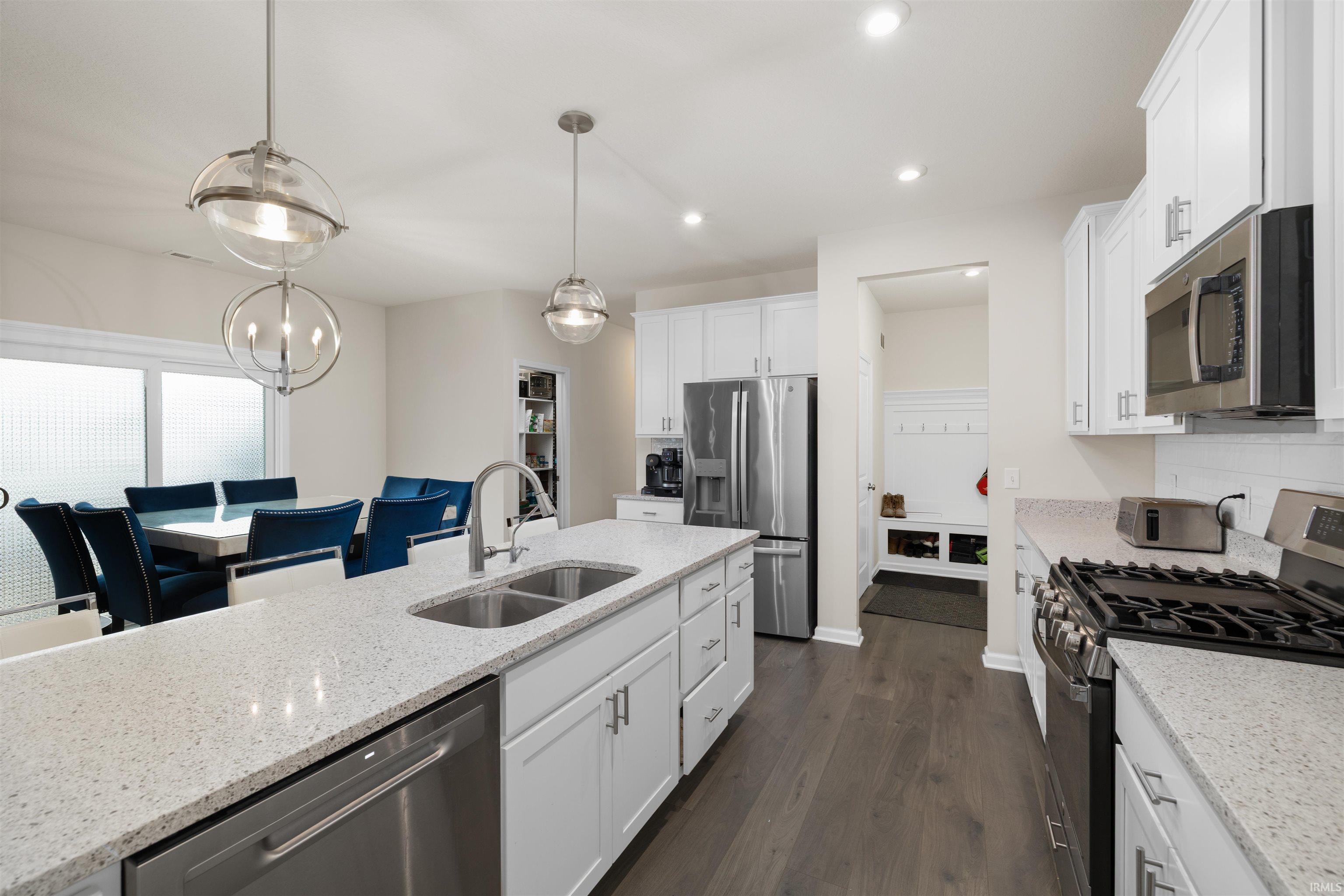 Kitchen featuring stainless steel appliances, white cabinetry, dark wood finished floors, light stone countertops, and suspended lighting