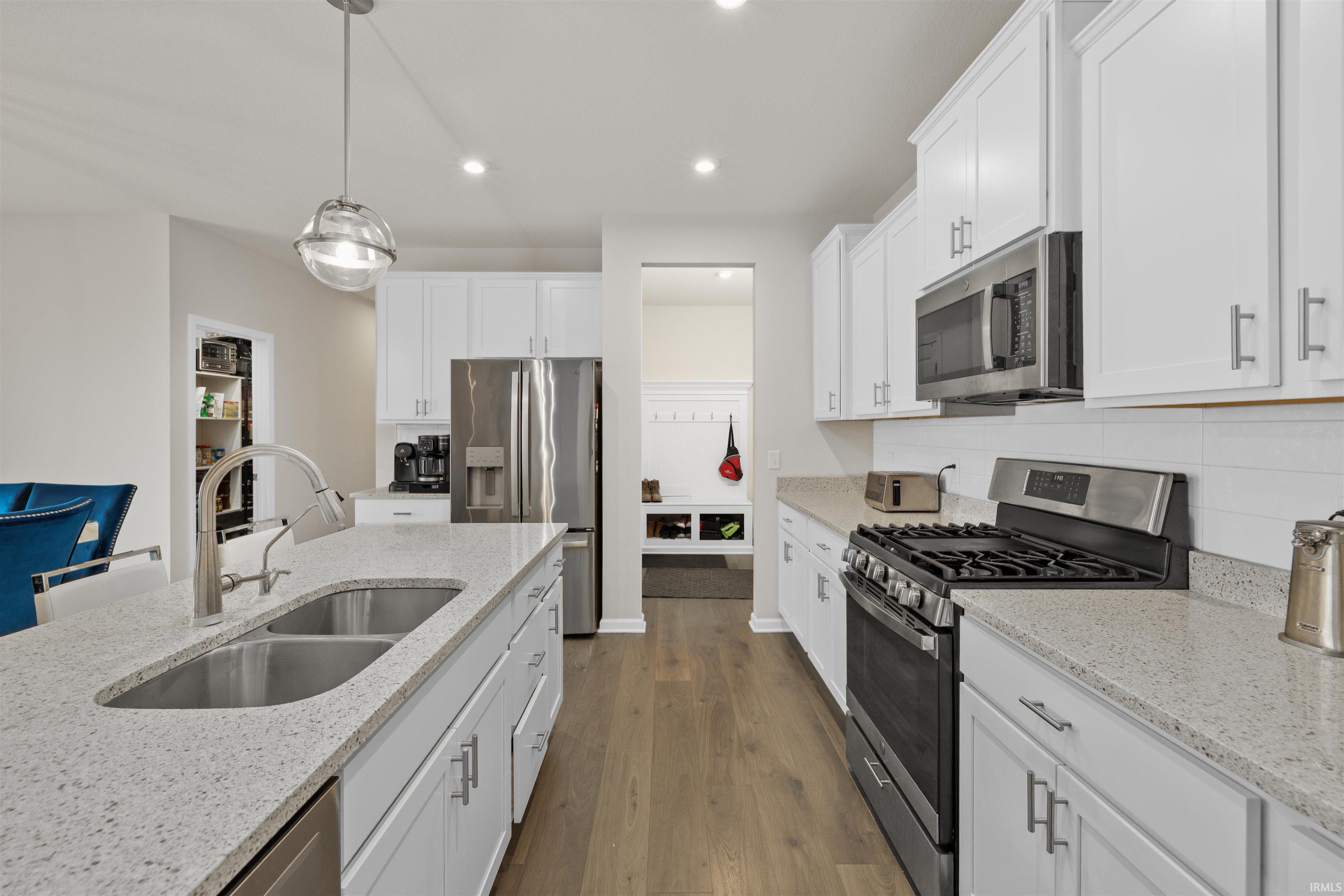Kitchen featuring stainless steel appliances, white cabinetry, dark wood-type flooring, decorative light fixtures, and light stone counters