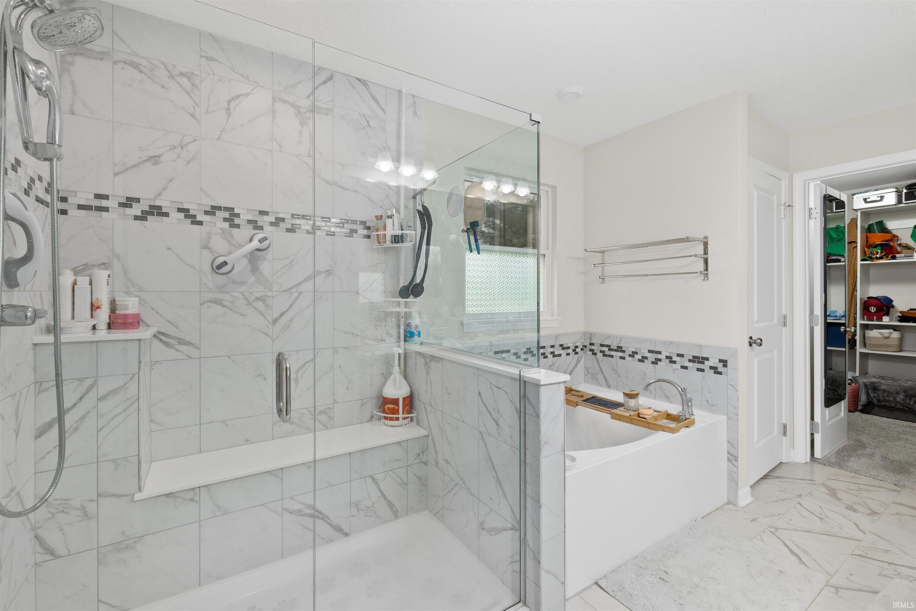 Full bath featuring light marble finish flooring, a stall shower, a bath, and a spacious closet