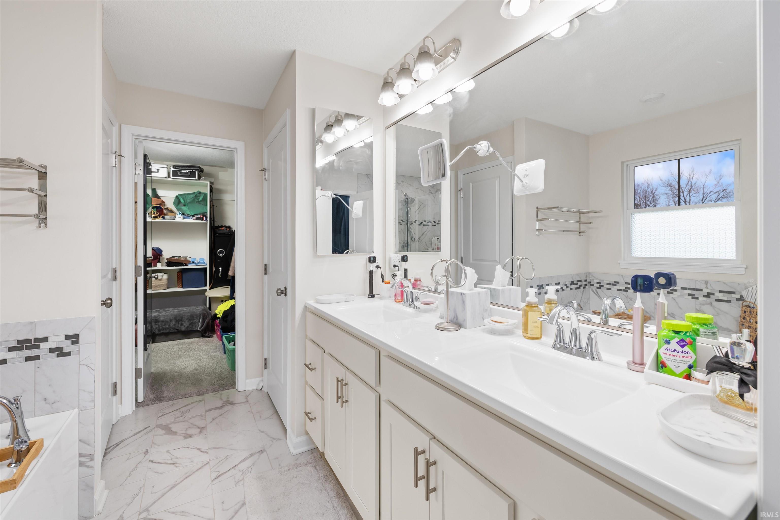 Bathroom featuring a bath, double vanity, and light marble finish flooring