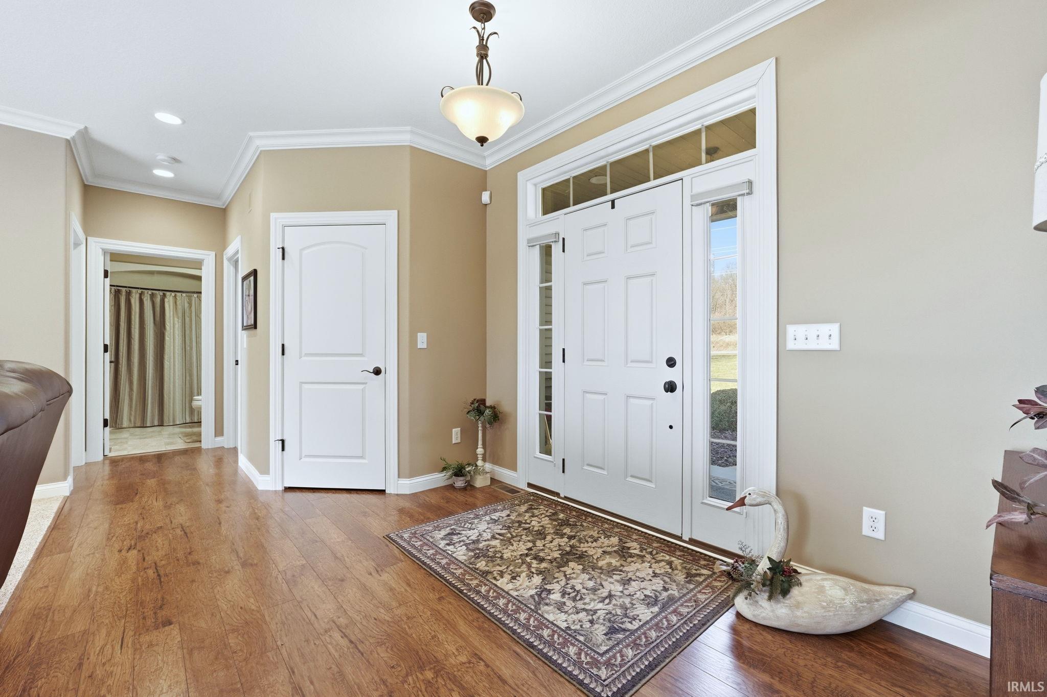 Foyer with ornamental molding, light wood finished floors, and recessed lighting