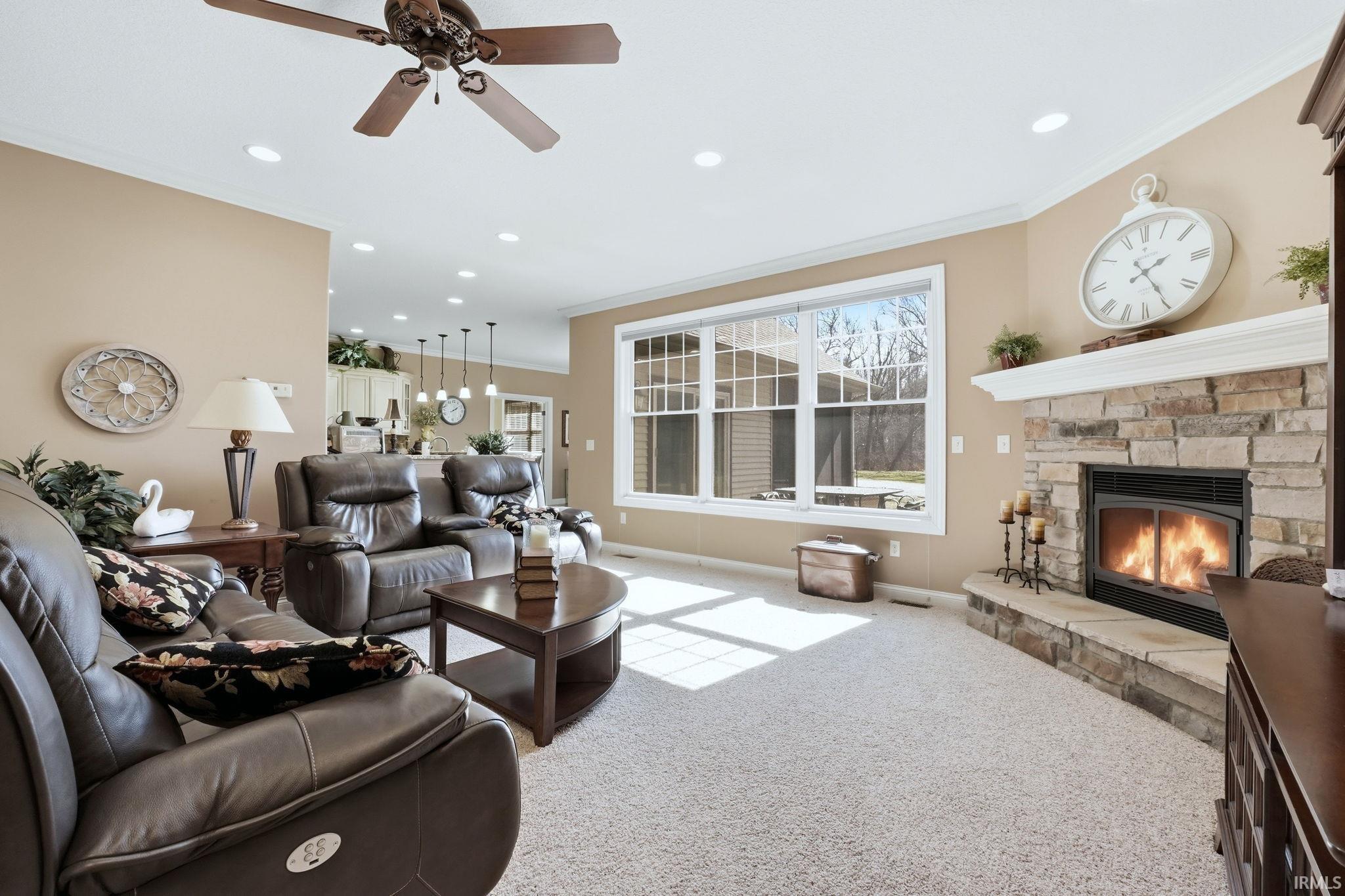 Living room with a ceiling fan, a fireplace, light colored carpet, ornamental molding, and recessed lighting