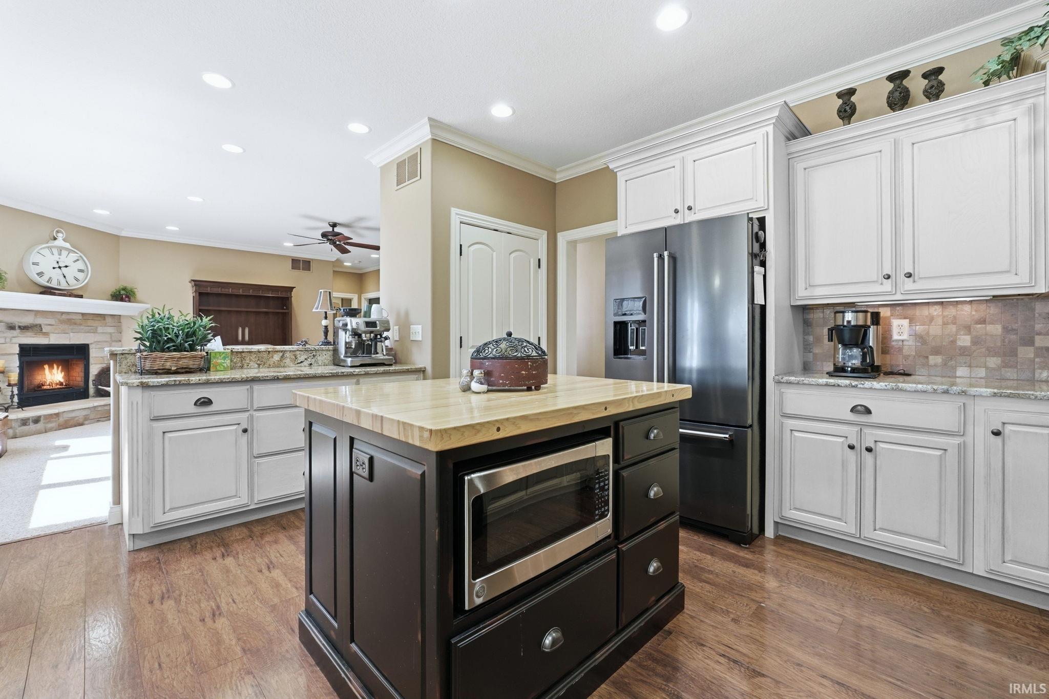 Two tone kitchen featuring a stone fireplace, ornamental molding, stainless steel appliances, a center island, and open floor plan