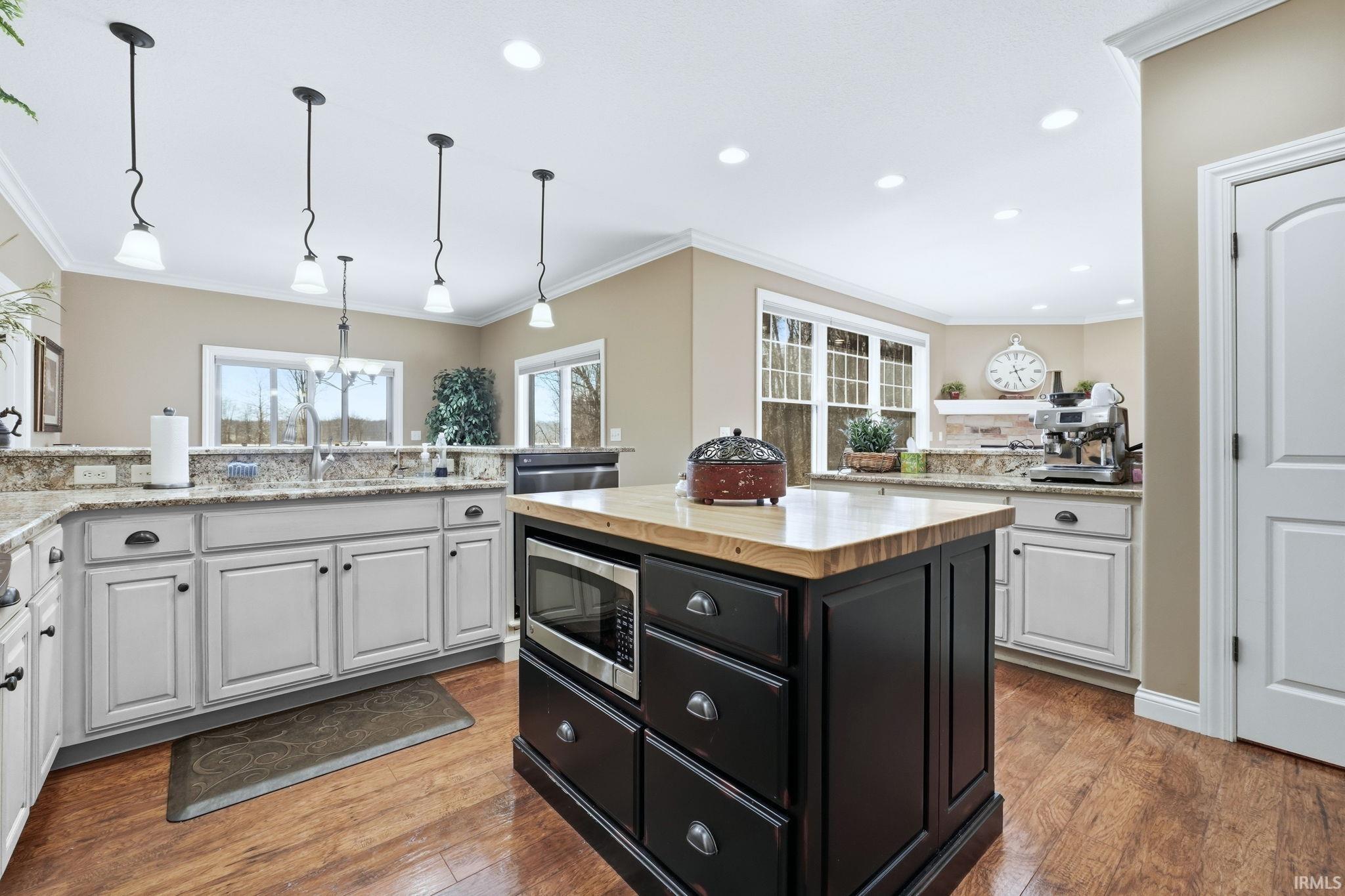 Two tone kitchen featuring a center island, crown molding, wooden counters, stainless steel microwave, and dark wood-style flooring
