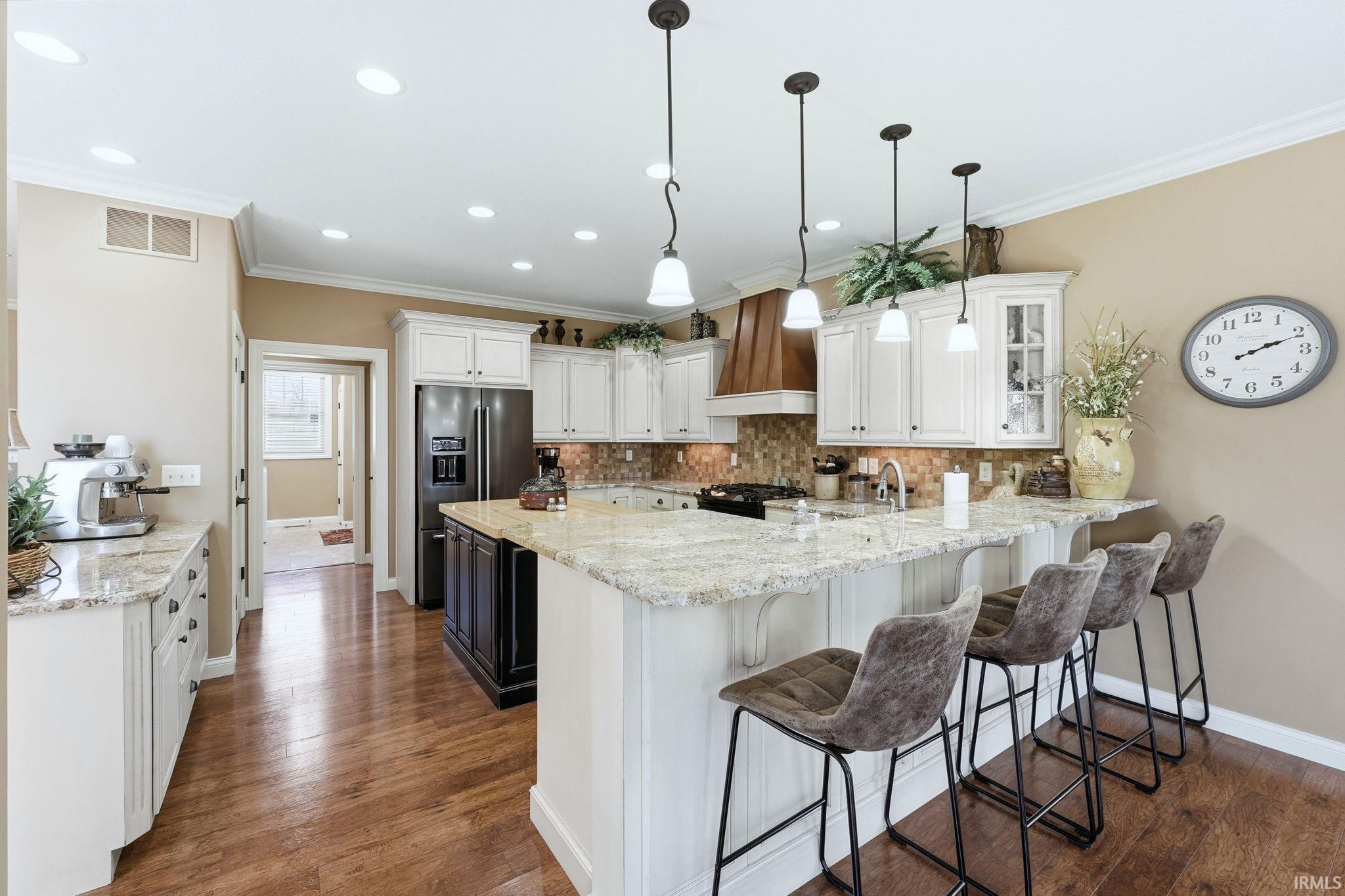 Two tone kitchen featuring light stone counters, a kitchen breakfast bar, a peninsula, glass fronted cabinets, and hanging light fixtures