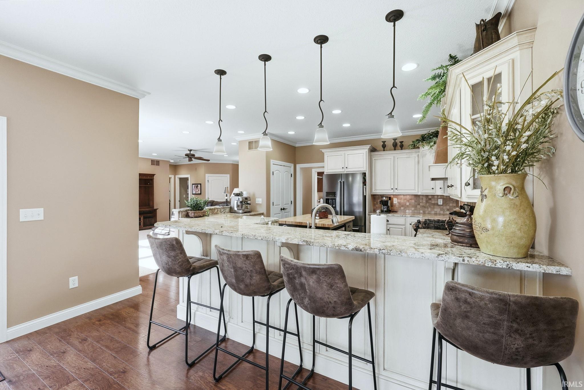 Kitchen with light stone countertops, a kitchen bar, tasteful backsplash, dark wood-style flooring, and hanging light fixtures