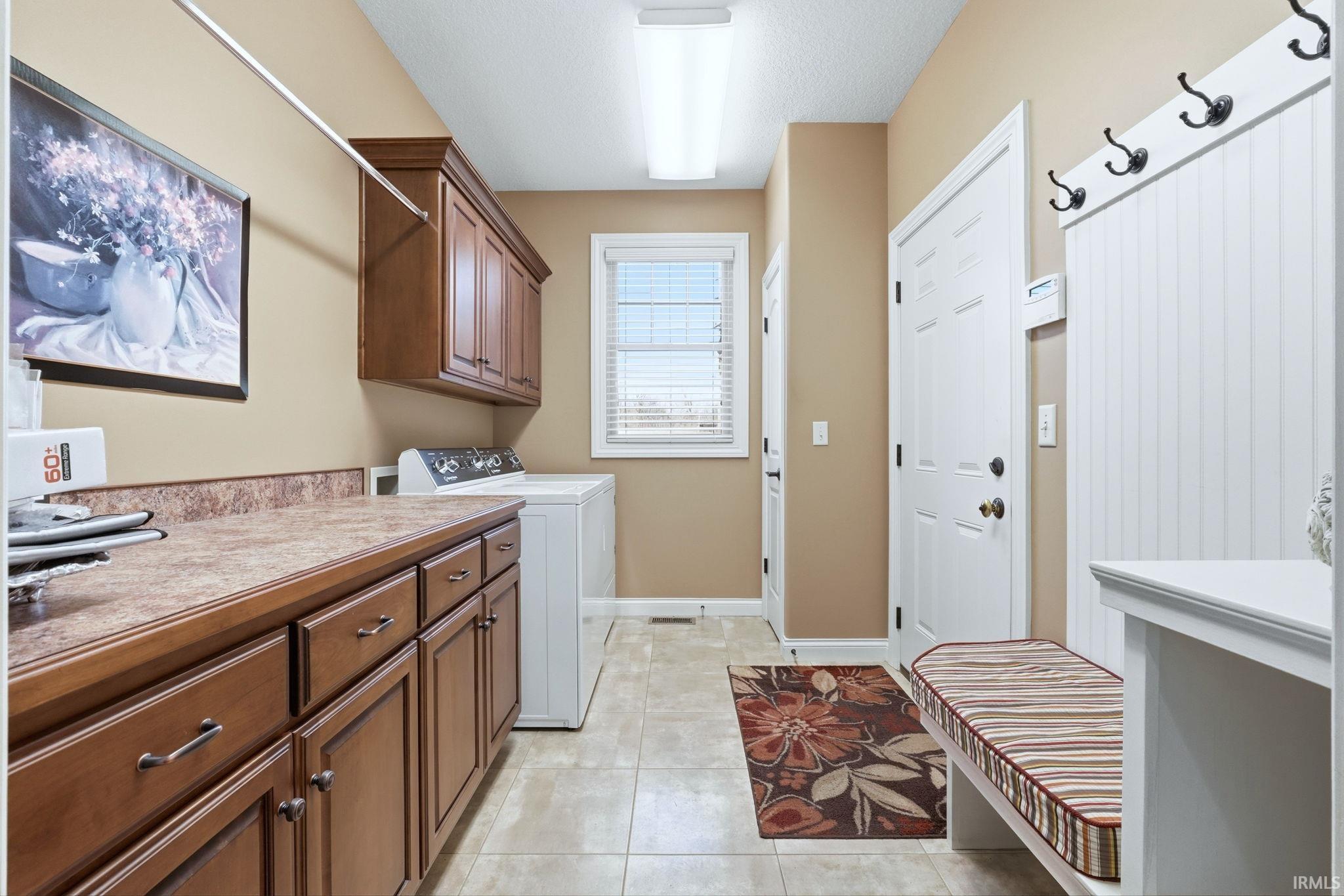 Laundry area with cabinet space, washing machine and clothes dryer, light tile patterned floors, and a textured ceiling
