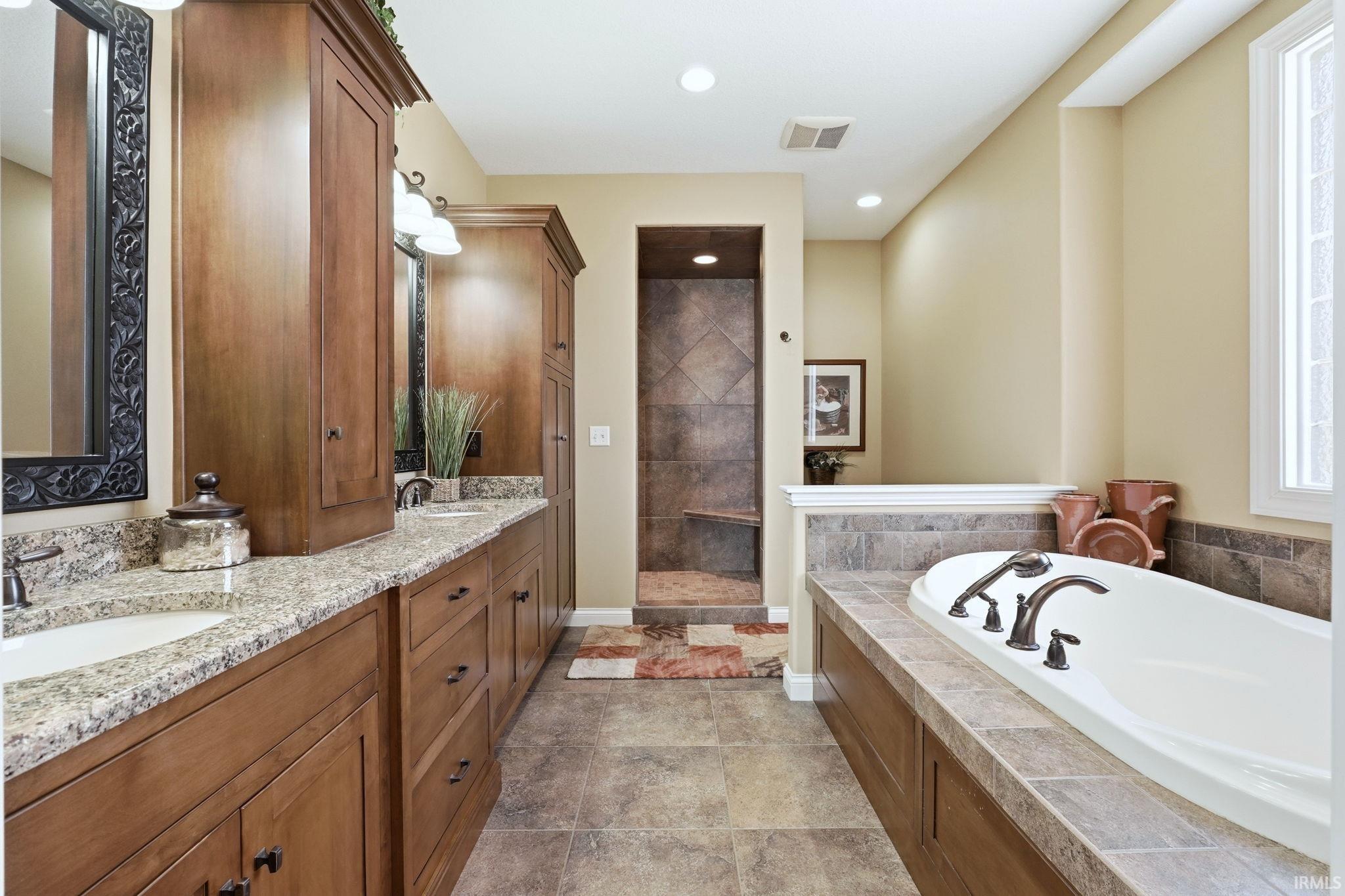 Full bathroom featuring double vanity, a walk in shower, a bath, and recessed lighting