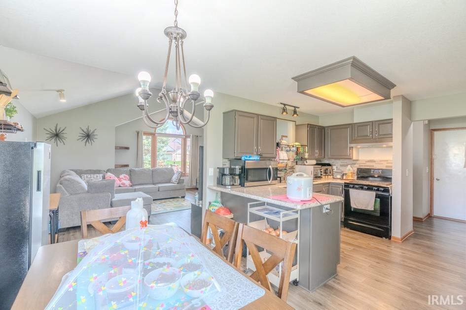 Kitchen with gray cabinets, stainless steel appliances, open floor plan, hanging lights, and light wood-style flooring