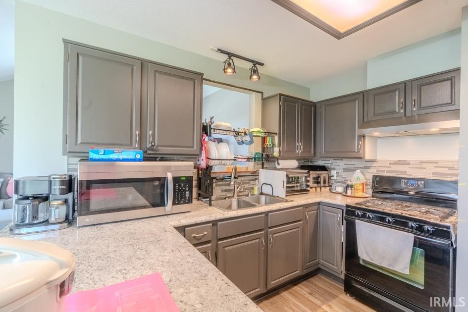 Kitchen featuring black gas range, gray cabinets, stainless steel microwave, light stone countertops, and tasteful backsplash