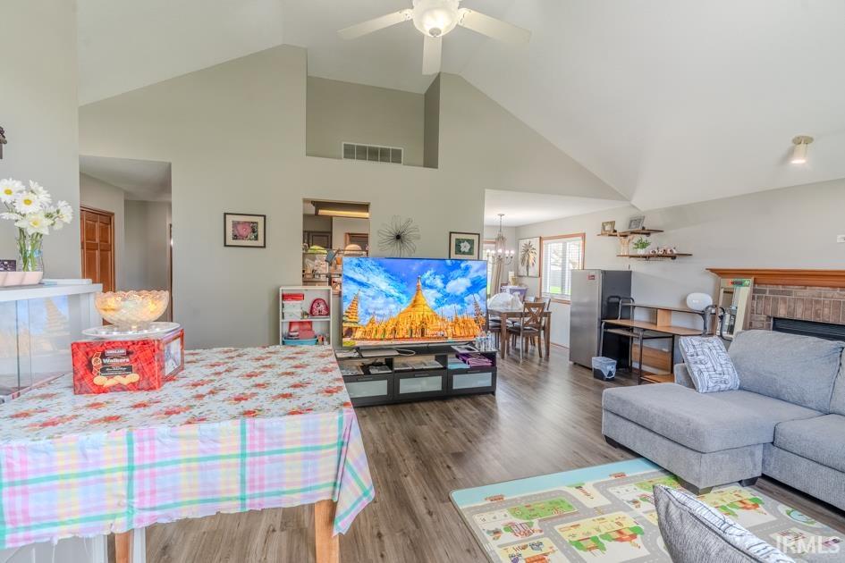 Living room with wood finished floors, vaulted ceiling, a ceiling fan, and a fireplace
