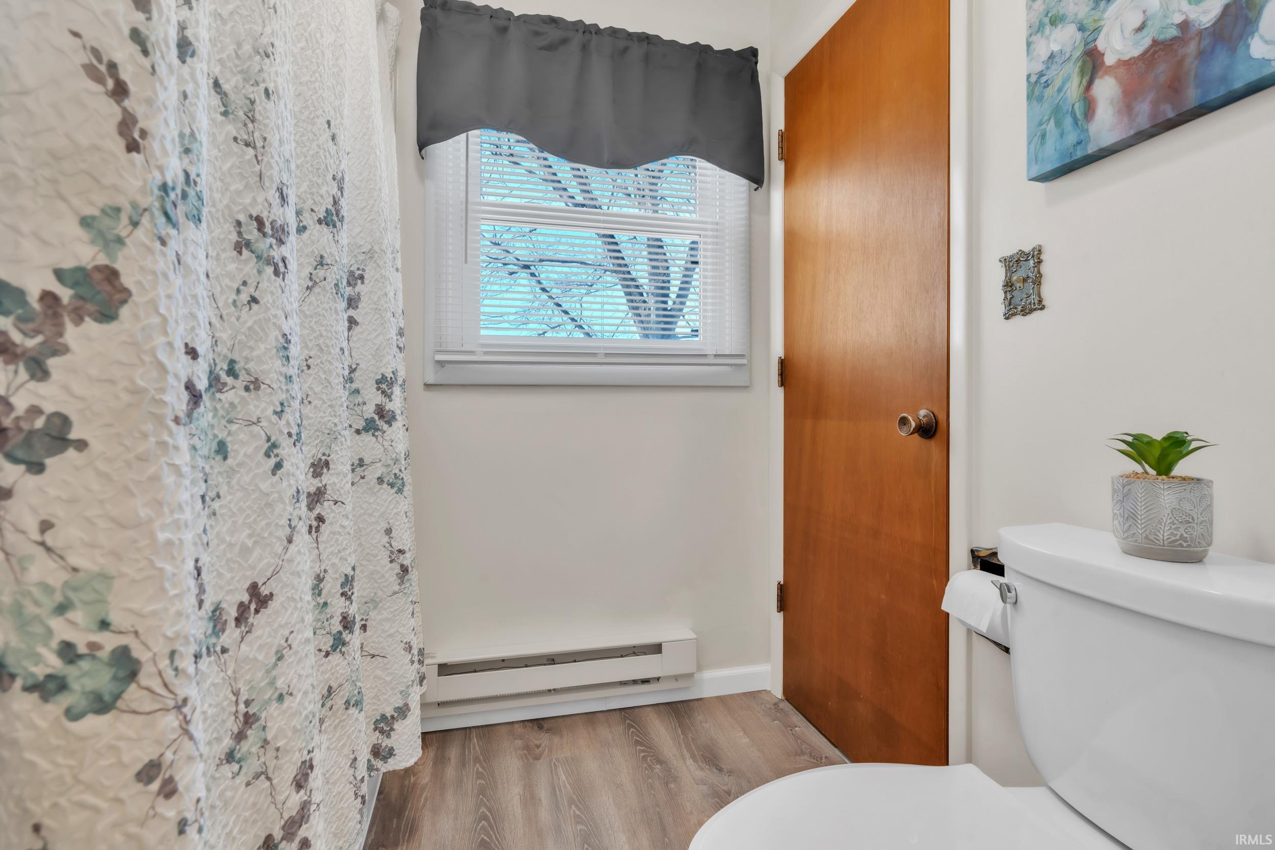 Full bathroom featuring a shower with shower curtain, a baseboard heating unit, and light wood finished floors