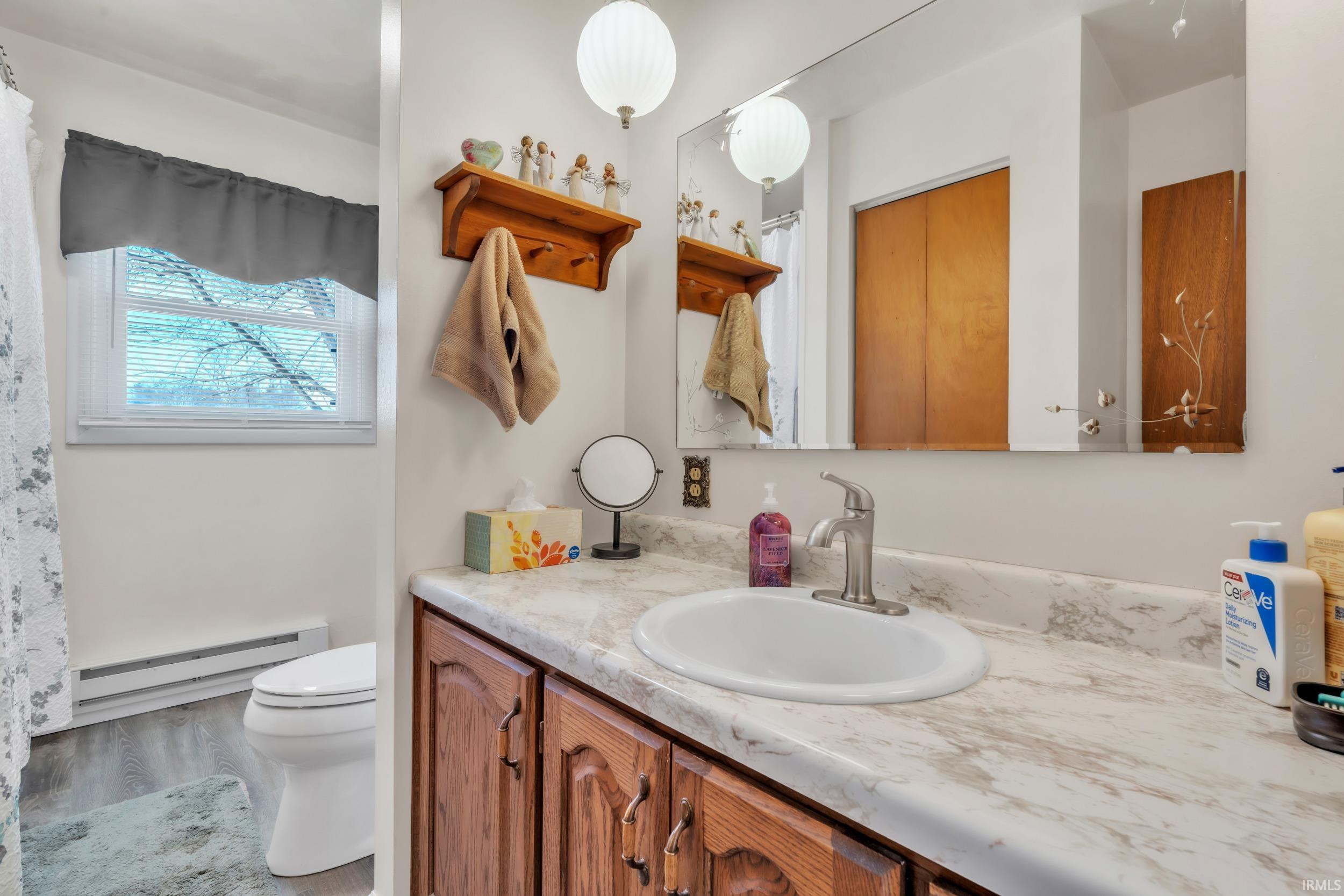 Full bathroom featuring vanity, a baseboard heating unit, a shower with curtain, and wood finished floors