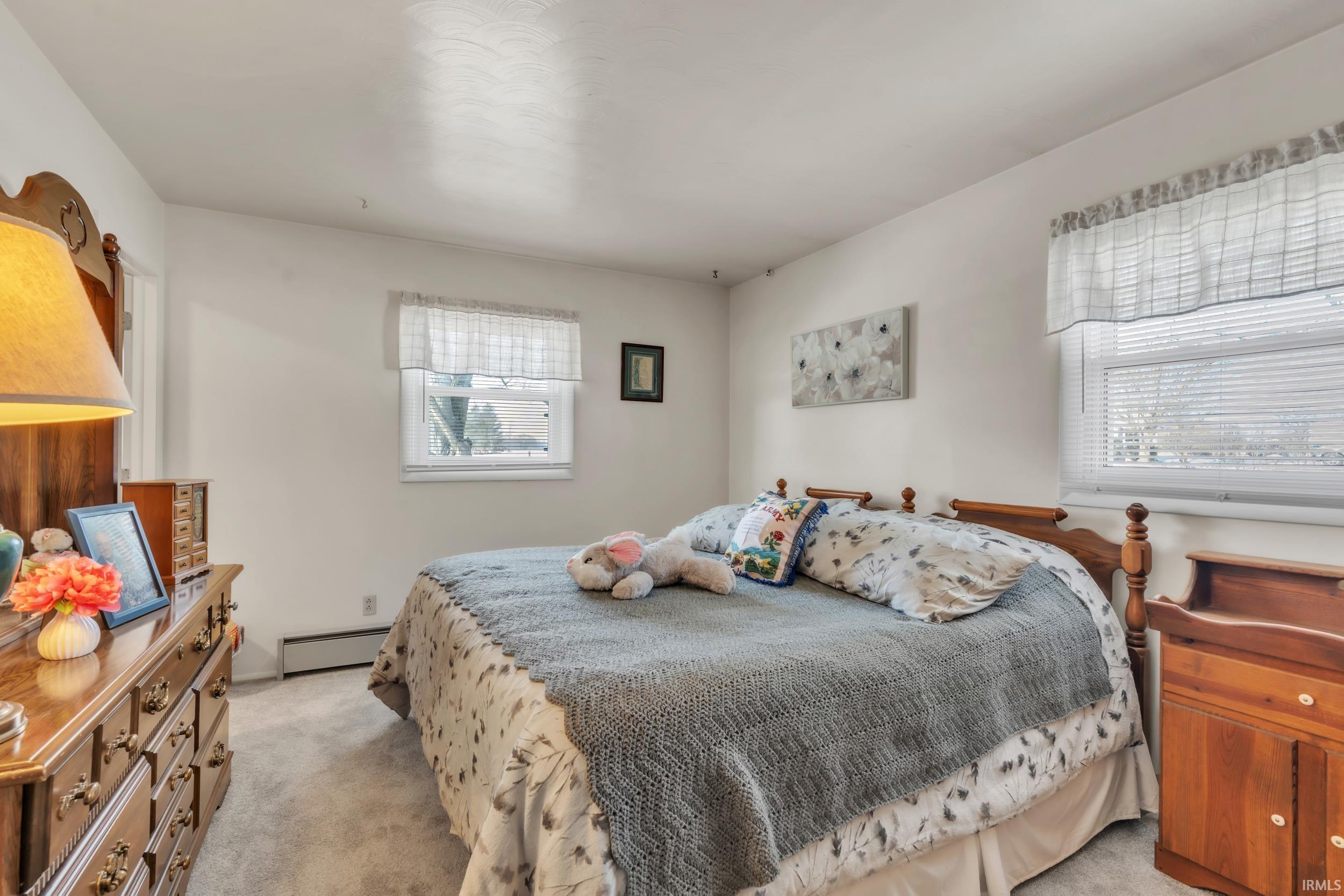 Bedroom with light colored carpet and a baseboard heating unit