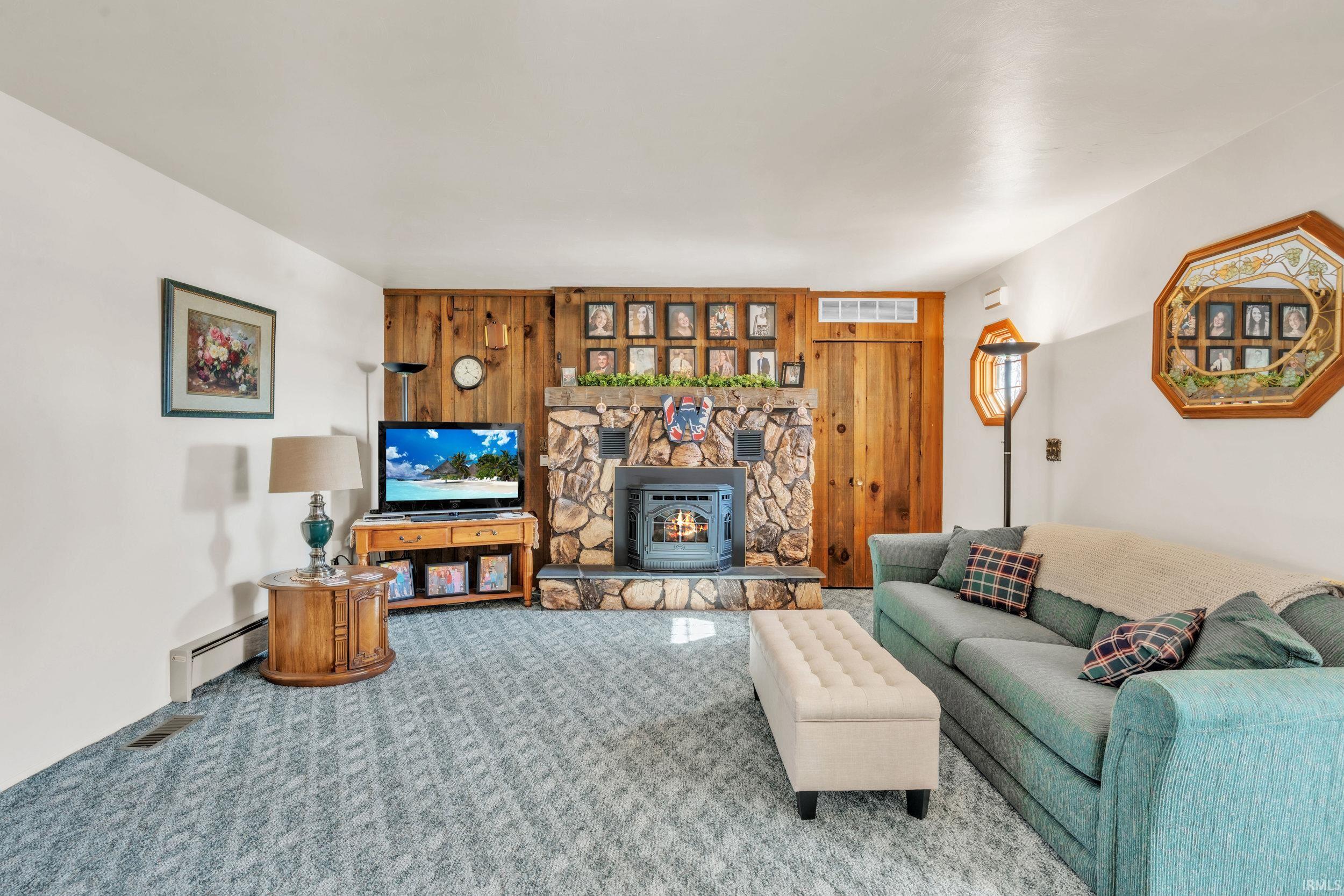 Living area with baseboard heating, carpet, and a wood stove