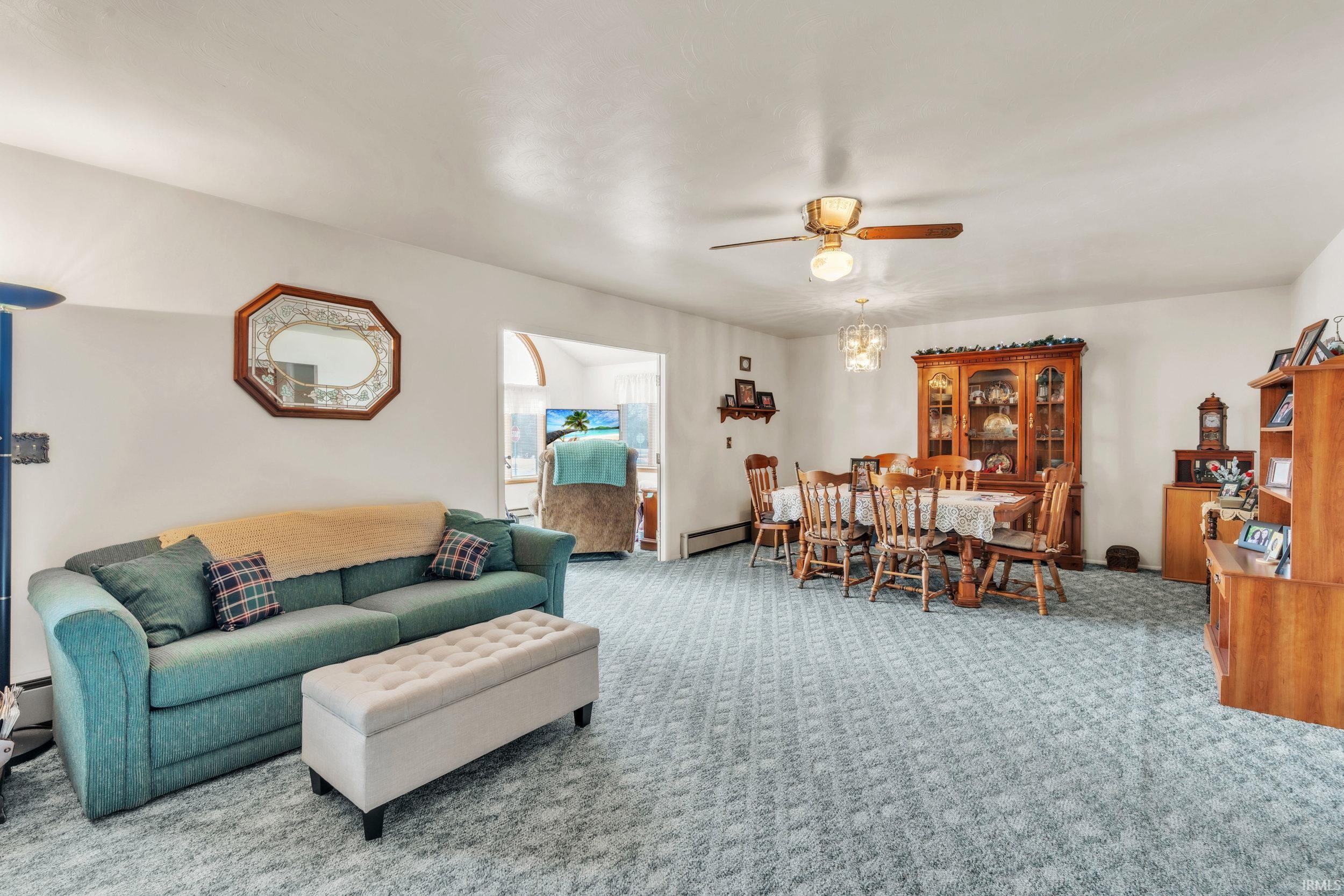 Carpeted living room featuring ceiling fan, baseboard heating, and a baseboard heating unit