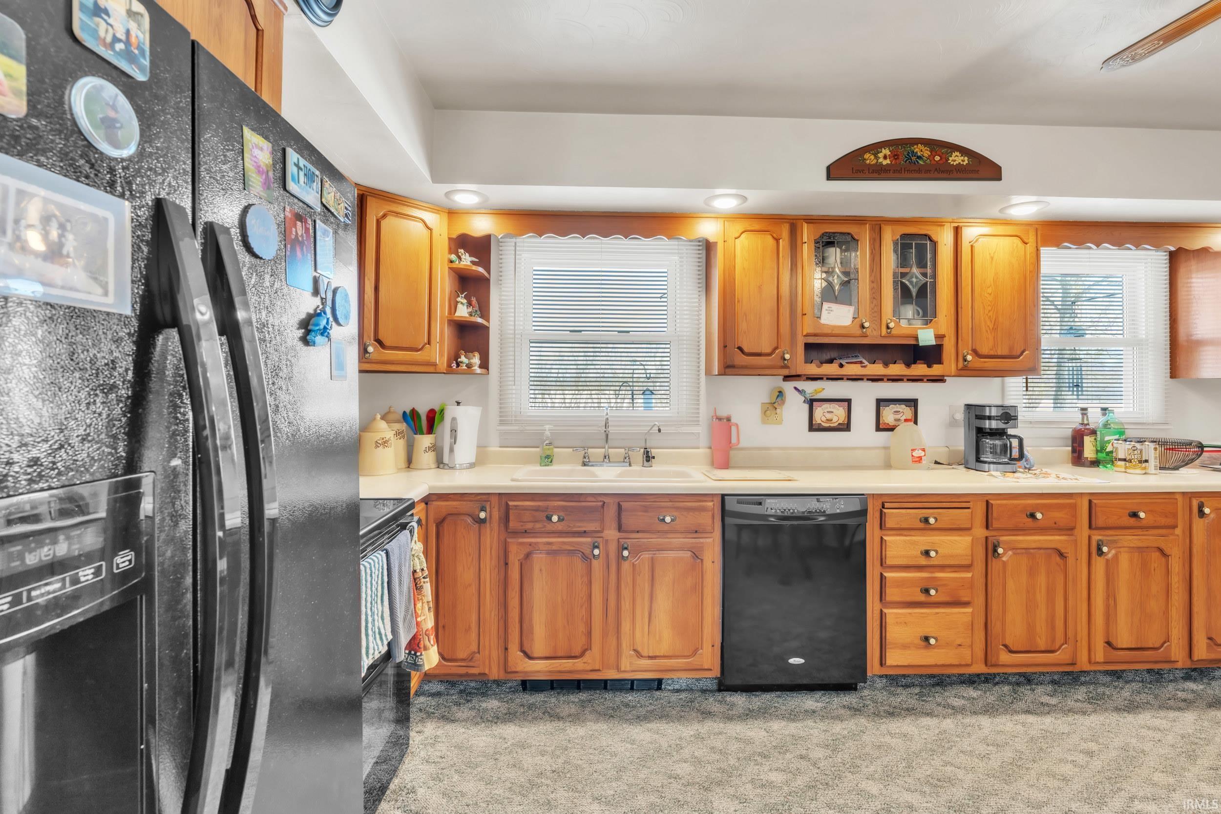 Kitchen with black appliances, light countertops, glass insert cabinets, open shelves, and wood finish cabinetry