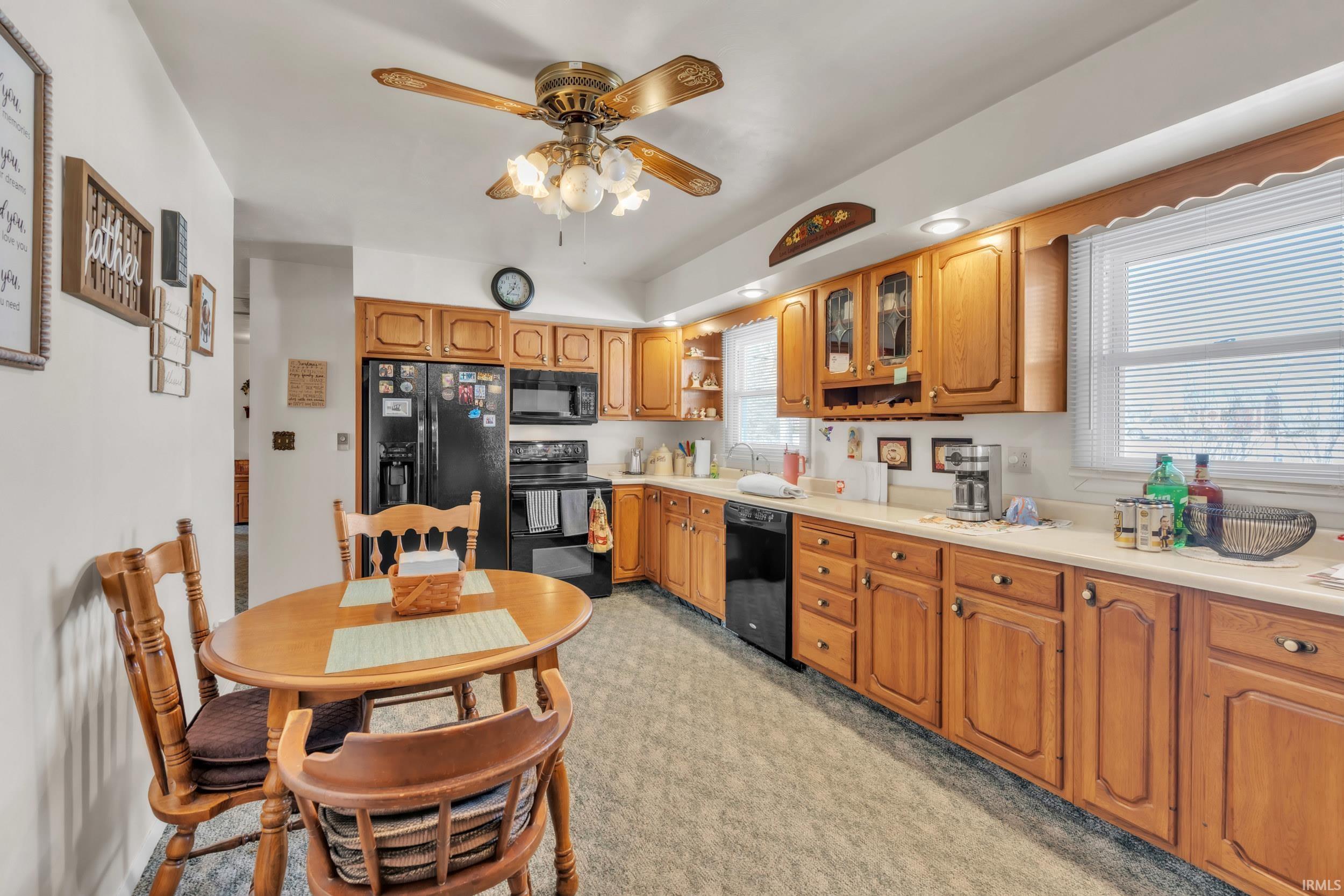 Kitchen with light countertops, black appliances, a ceiling fan, glass insert cabinets, and wood finish cabinets