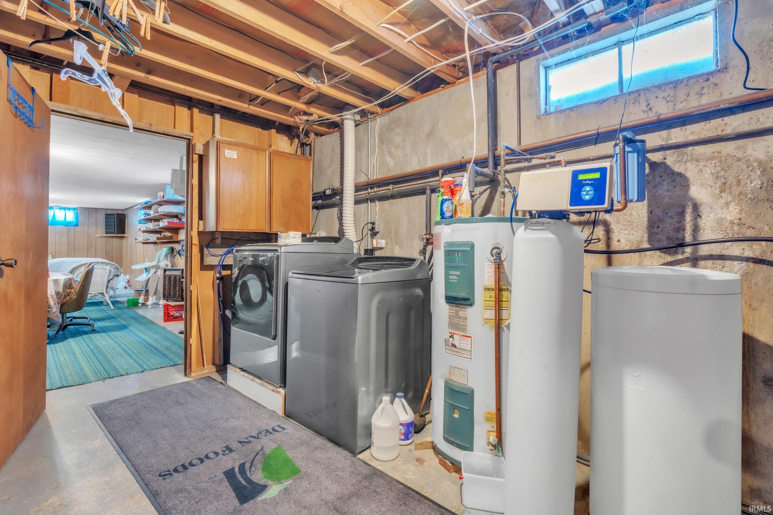Laundry room with concrete flooring, water heater, washing machine and clothes dryer, and cabinet space