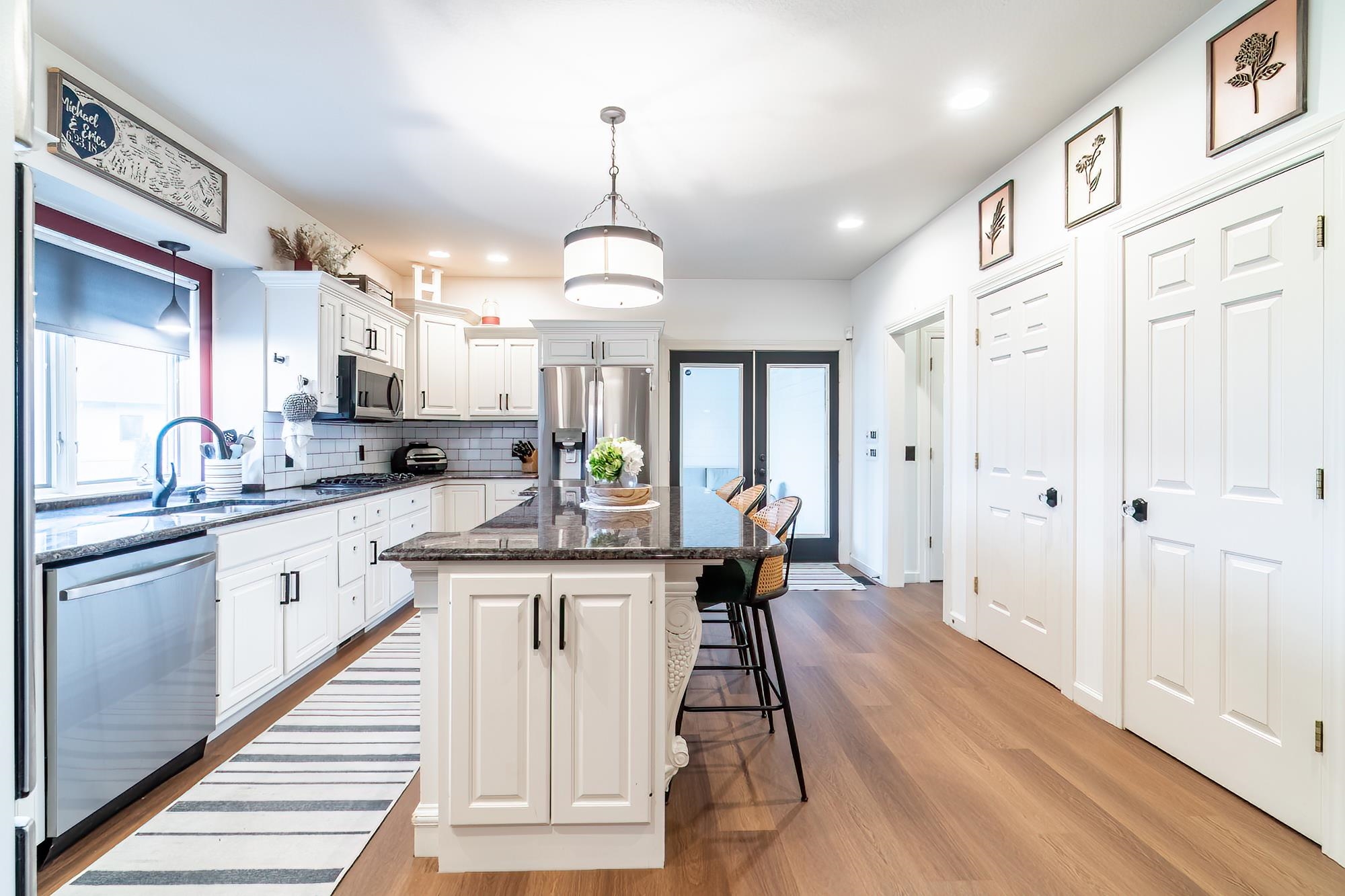 Kitchen with white cabinets, dark stone counters, stainless steel appliances, and light wood-style flooring