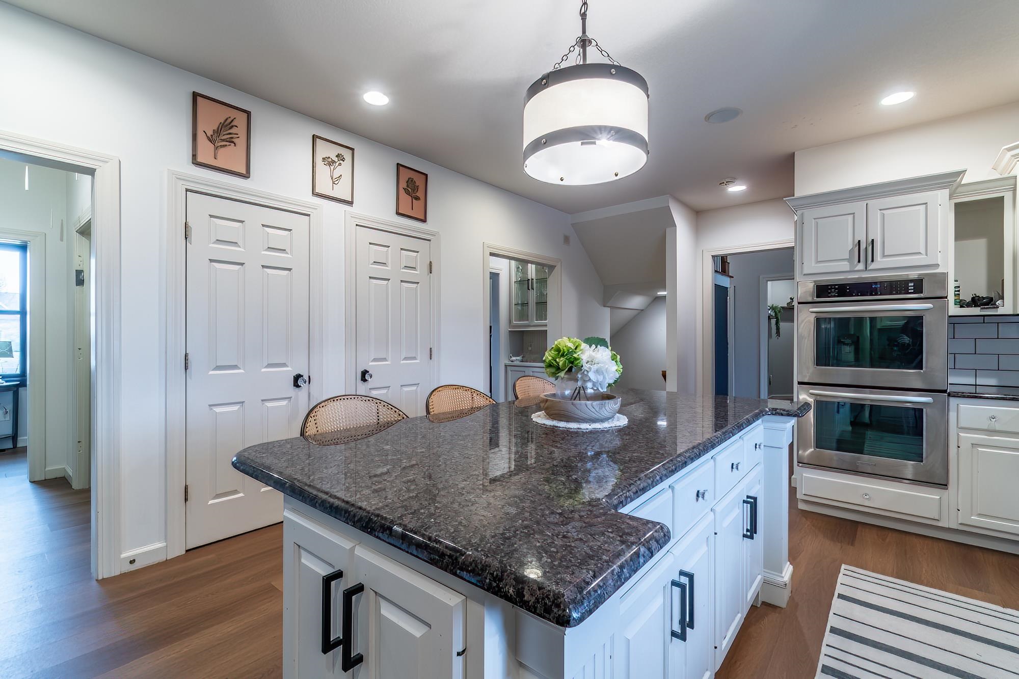 Kitchen featuring stainless steel double oven, dark stone counters, a center island, dark wood-style flooring, and a breakfast bar