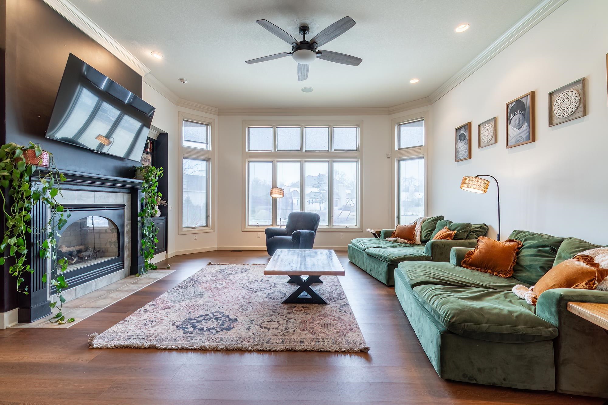 Living area featuring a fireplace, crown molding, dark wood-style floors, a ceiling fan, and plenty of natural light