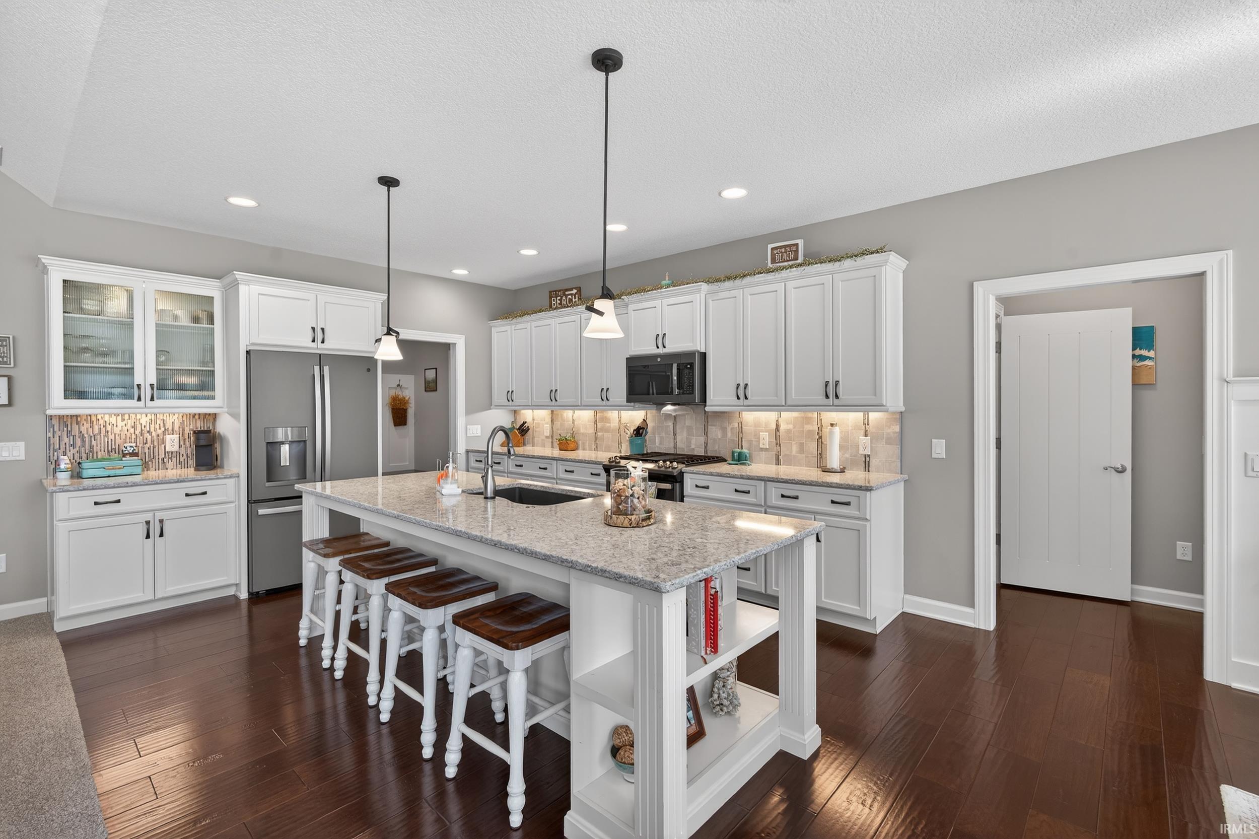 Kitchen featuring white cabinets, light stone counters, tasteful backsplash, stainless steel appliances, and dark wood-style floors