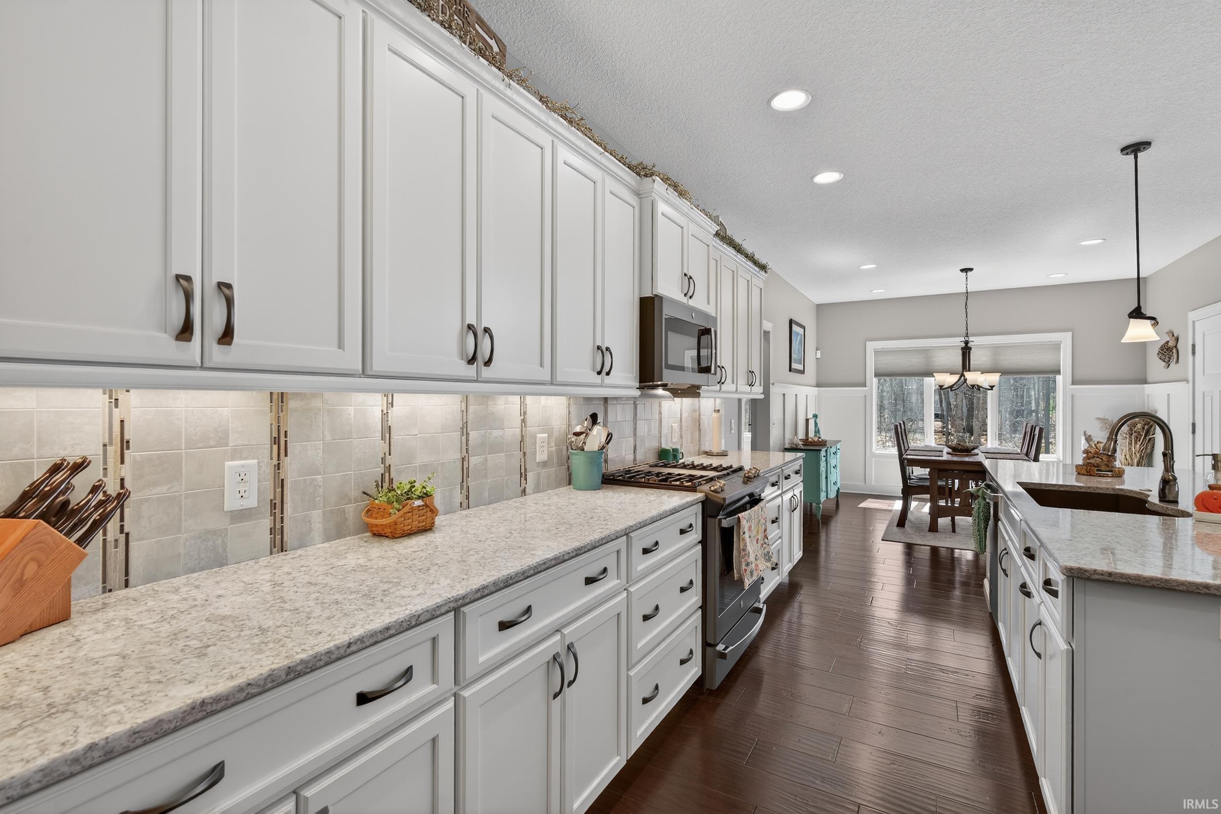Kitchen with white cabinetry, light stone counters, stainless steel appliances, dark wood finished floors, and hanging lights