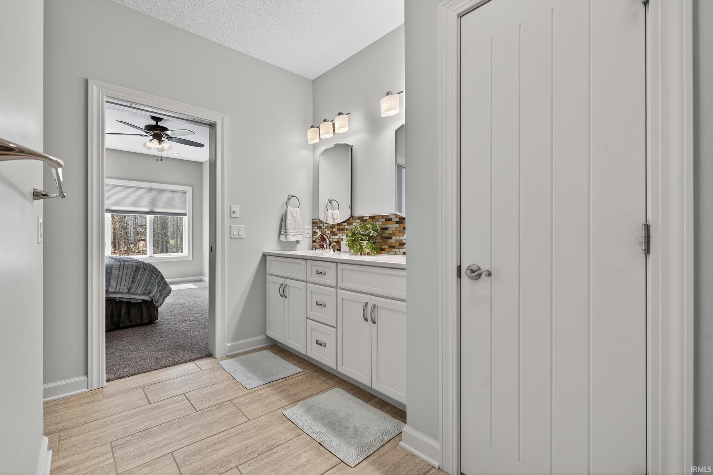 Ensuite bathroom featuring double vanity, wood tiled floors, decorative backsplash, ceiling fan, and a textured ceiling
