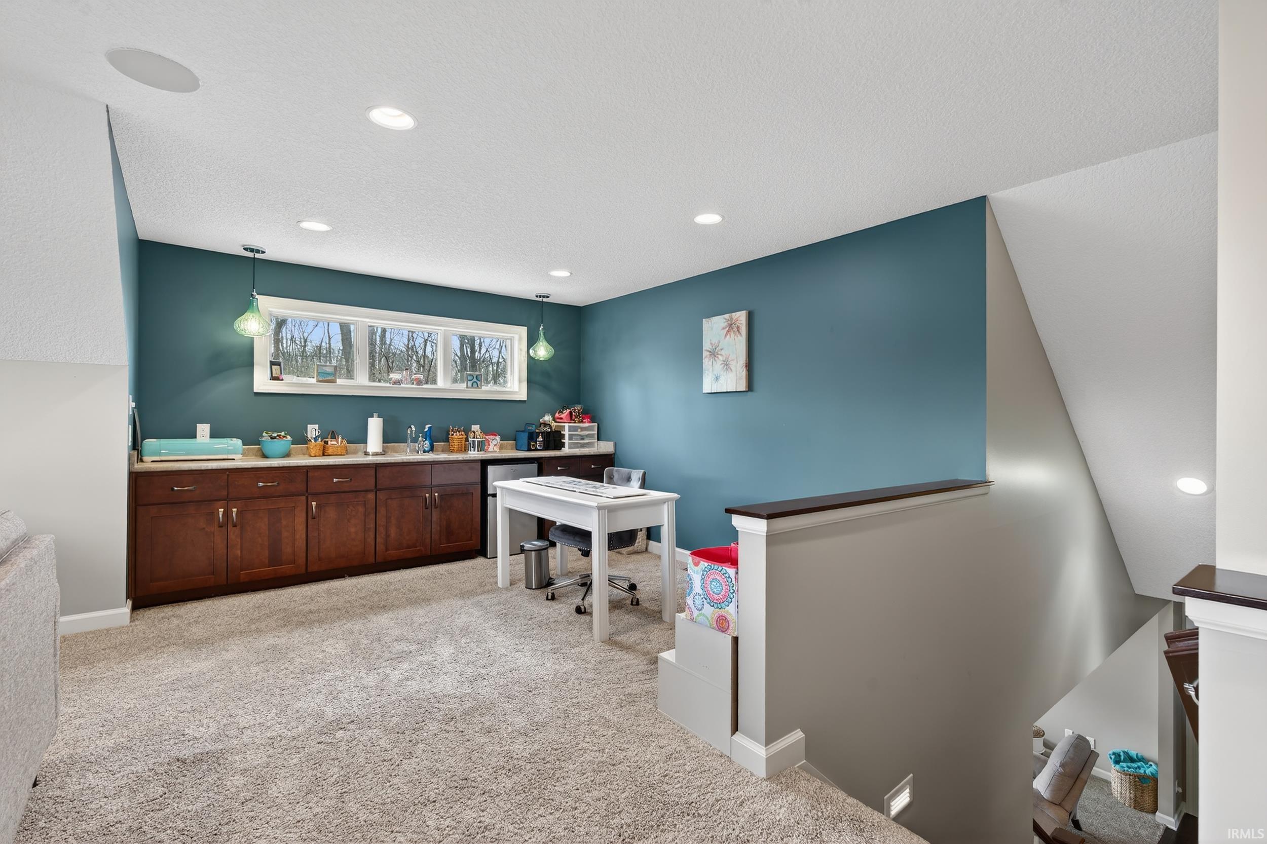 Bar with light colored carpet, light countertops, stainless steel fridge, a textured ceiling, and hanging light fixtures