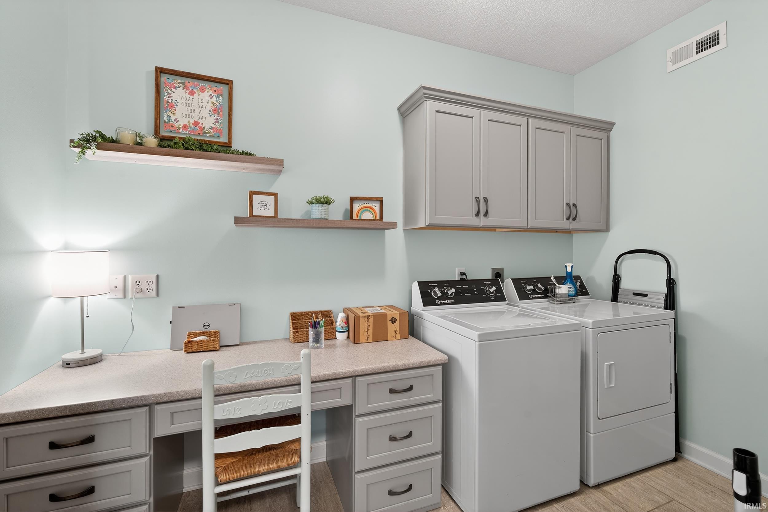 Laundry area featuring separate washer and dryer, a textured ceiling, light wood-type flooring, and cabinet space