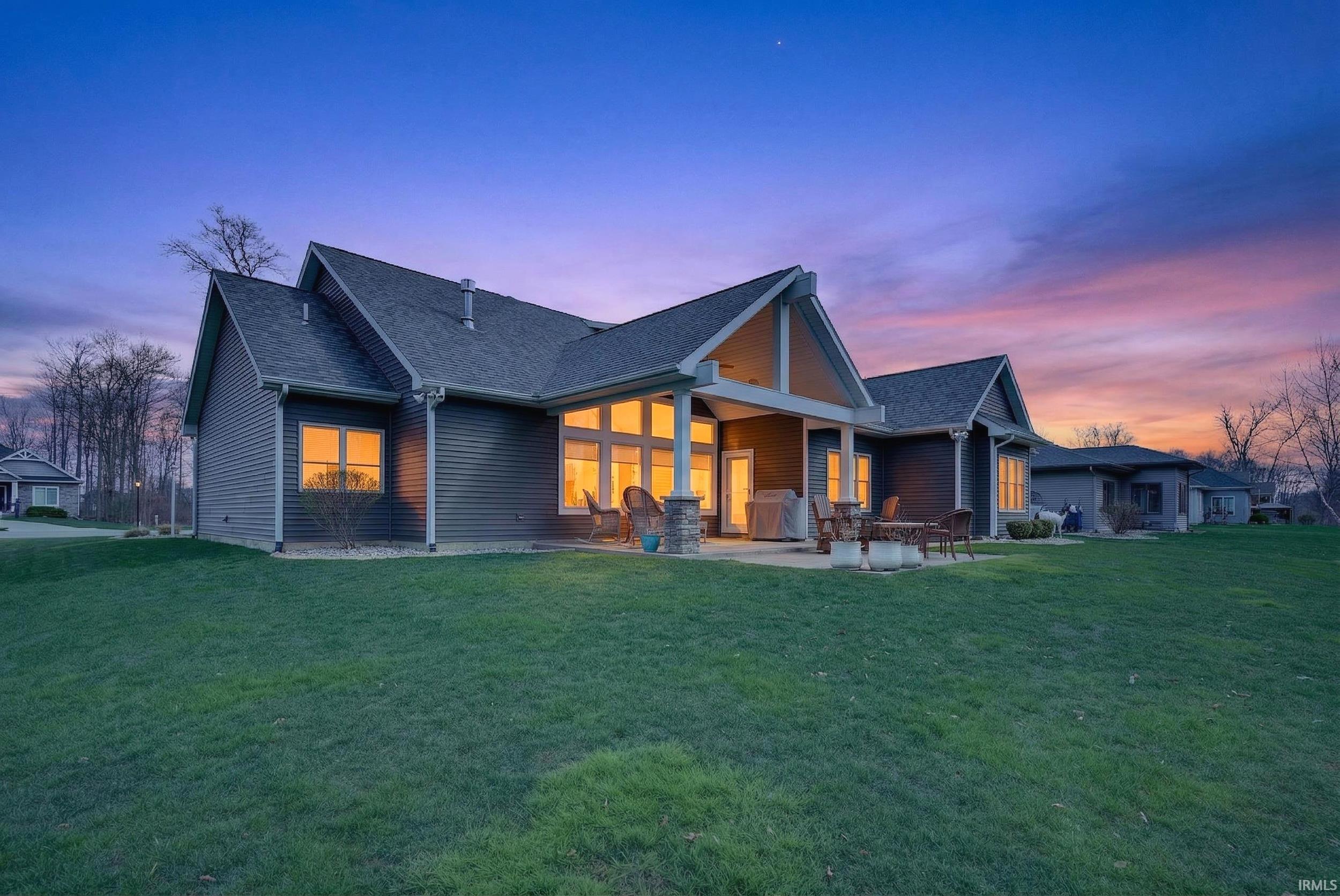 Back of house at dusk with a patio area, a lawn, and roof with shingles