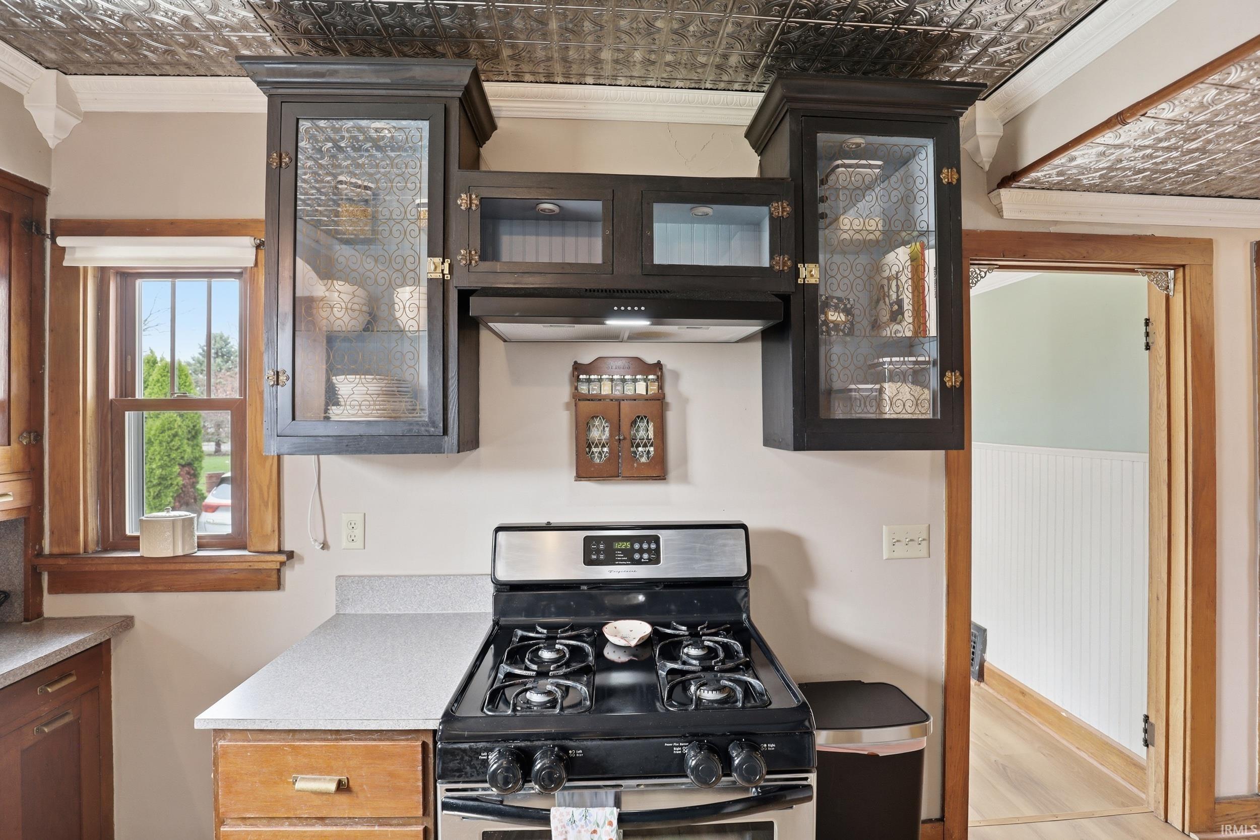 Kitchen with an ornate ceiling, crown molding, glass fronted cabinets, stainless steel gas stove, and exhaust hood