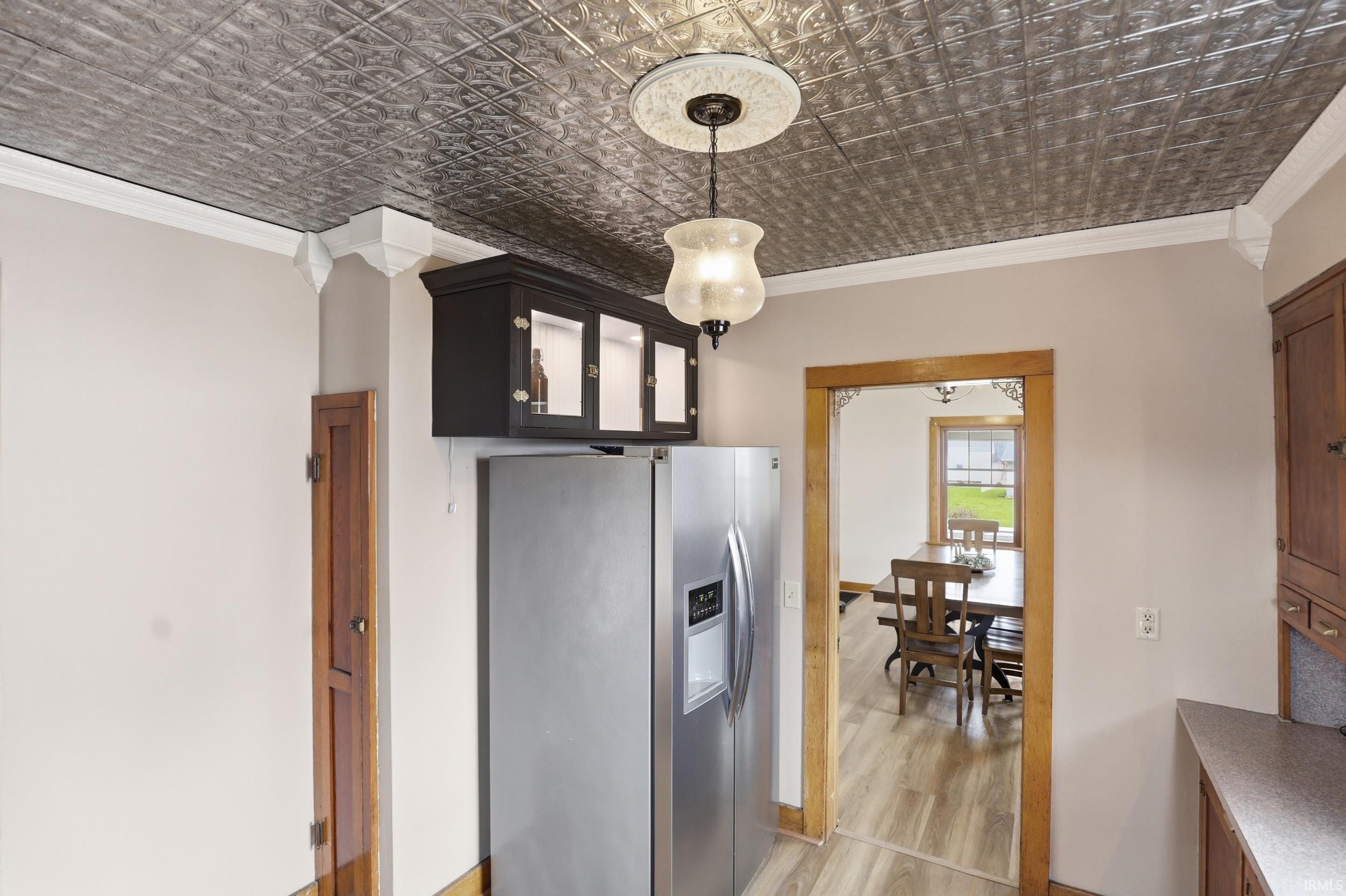 Kitchen featuring stainless steel fridge with ice dispenser, ornamental molding, light wood-style flooring, hanging light fixtures, and an ornate ceiling