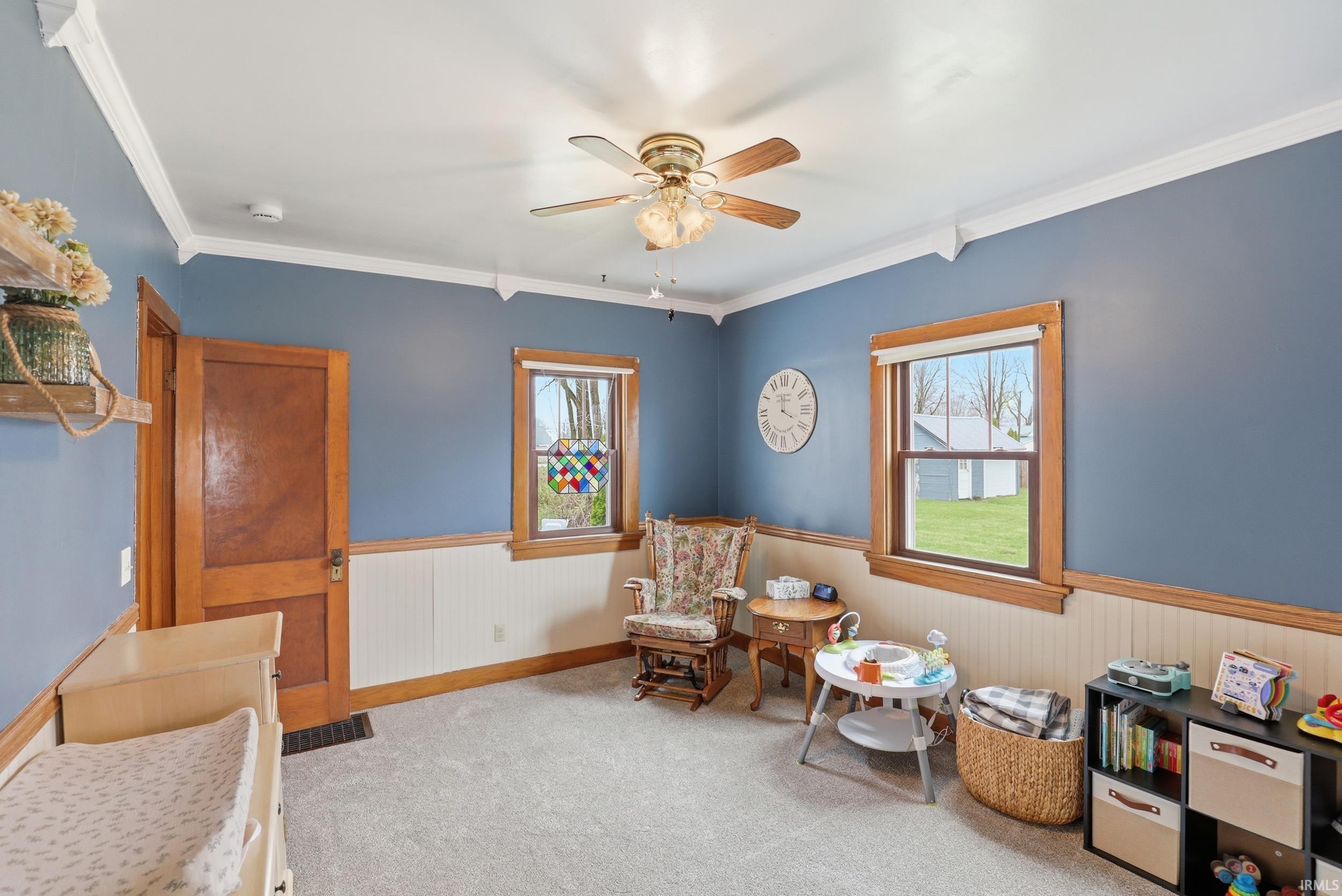 Bedroom featuring wainscoting, ornamental molding, light colored carpet, and a ceiling fan